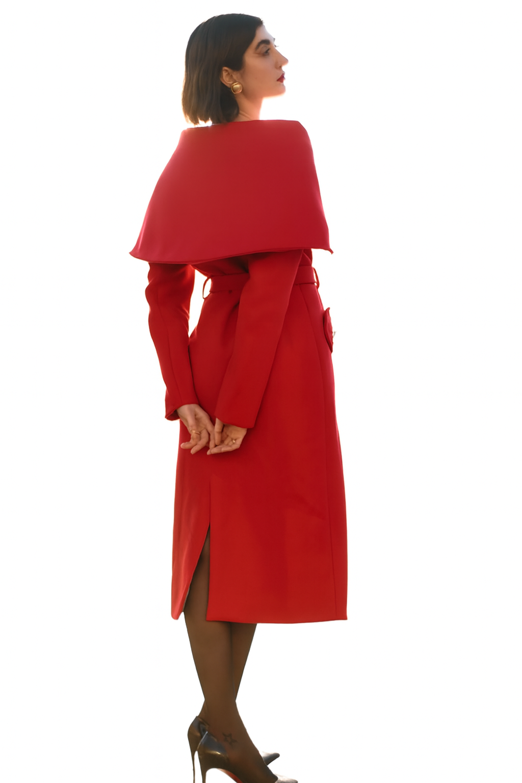 Femme élégante en robe longue rouge avec cape, chaussures à talons et collants noirs, posant de profil contre un fond blanc.