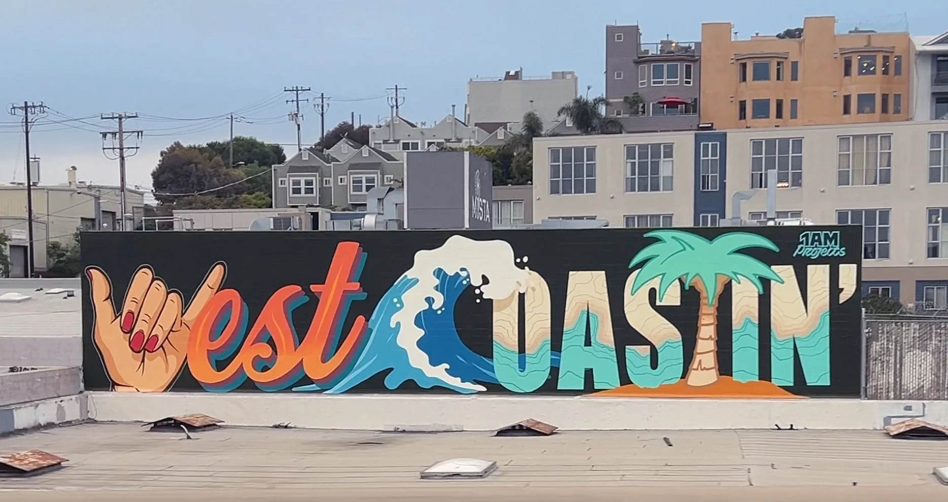 Colorful mural on a wall with a hand making a shaka sign, a wave, the word 'West' in orange, the word 'Vason' with a palm tree, and a small logo that says '1AM Projects' against a background of buildings and power lines.