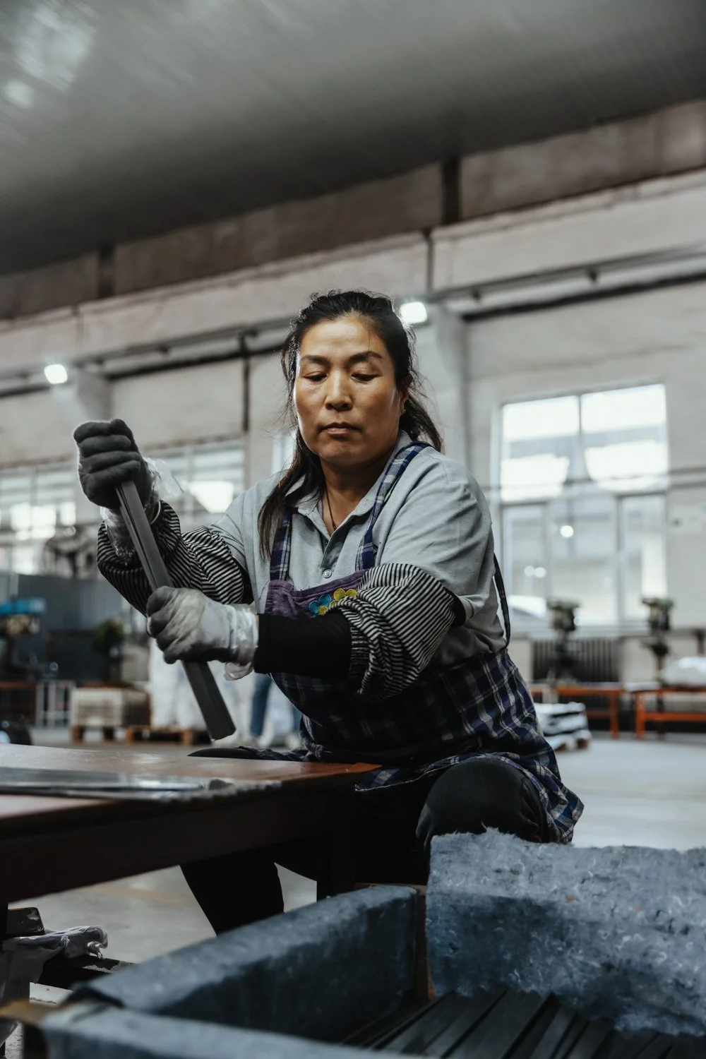 Frau arbeitet in einer Werkstatt, trägt Schutzkleidung und benutzt Werkzeug, um an einem Projekt zu arbeiten.
