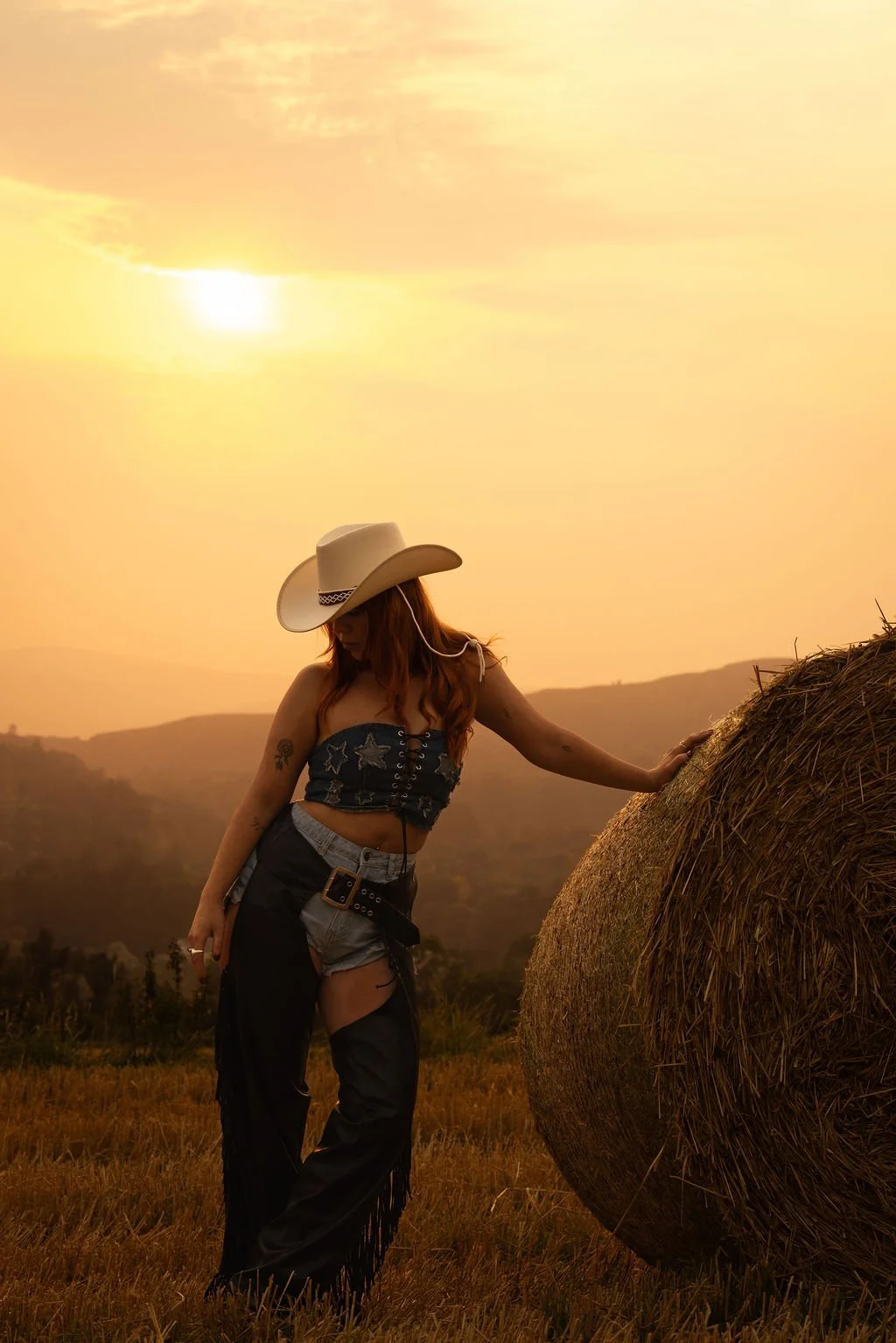 Sorcha in a cowboy hat standing beside a straw bale at sunset in rural Ireland