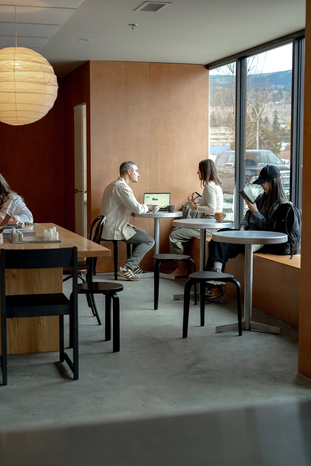 A customer with curly hair at a checkout counter in a retail store, smiling and holding a smartphone, with a smiling cashier behind the register