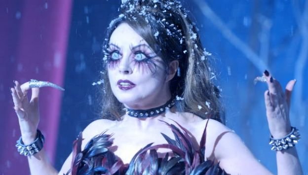 An image of a woman with bright eyes and extremely long eyelashes, covered in fake snow, with long pointed metal spikes on her nails