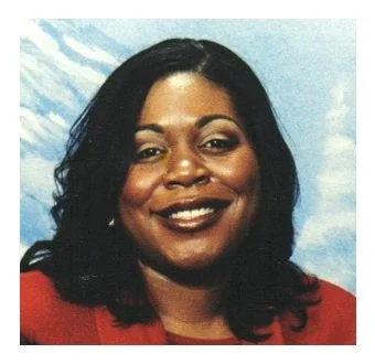 Portrait of a smiling woman with dark hair, wearing red, against a partly cloudy sky background.