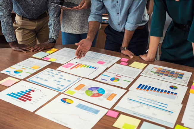 A collection of tools and charts related to data analysis and goal setting, including a blue rising bar graph on paper, a clipboard with checklists, a caliper, a ruler, a stopwatch, a blue card with a checkmark list, a roll of blue paper, and a target with an arrow.