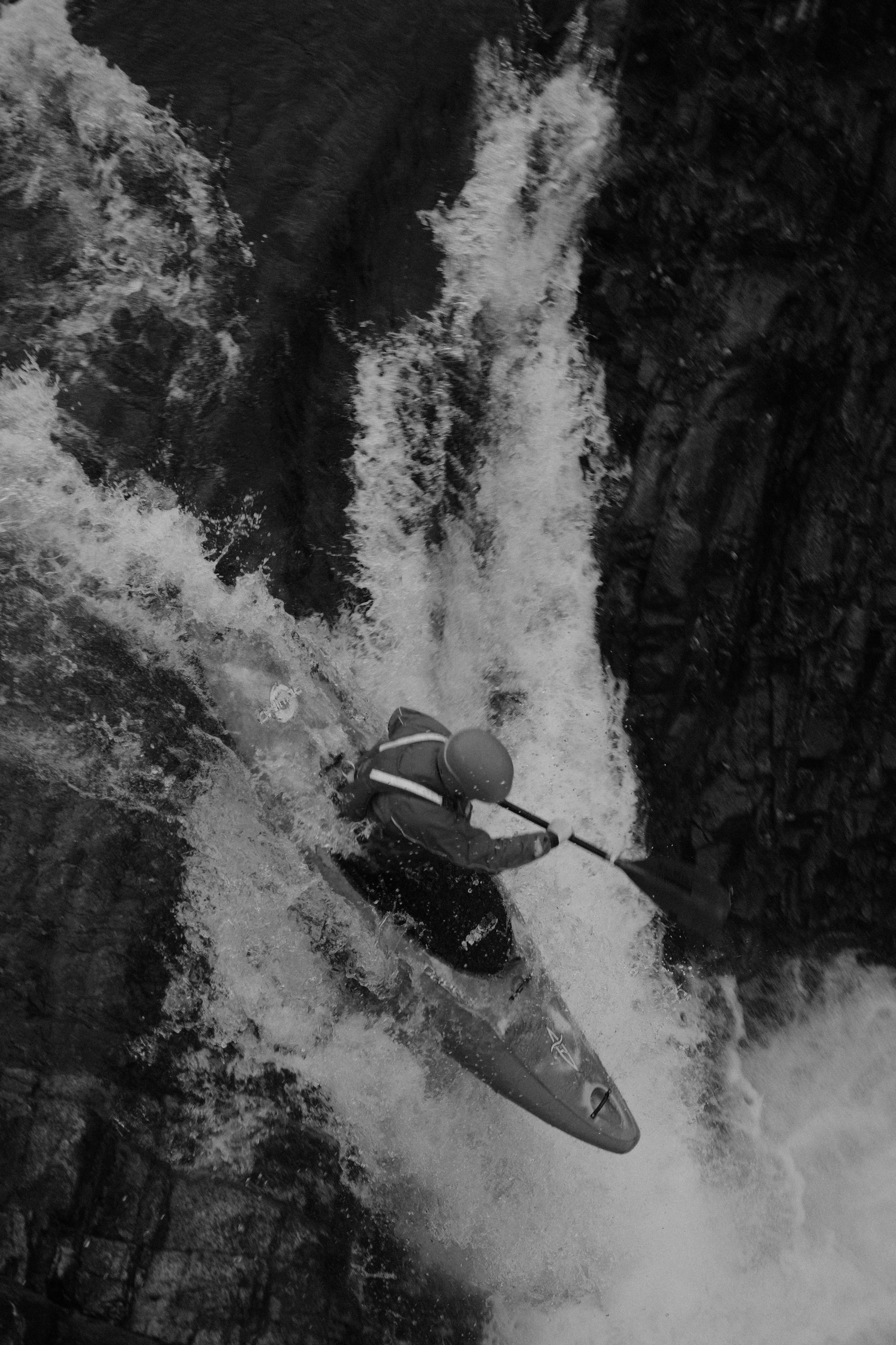 Un kayakiste pagayant dans une rivière en eaux vives, entouré de rochers.