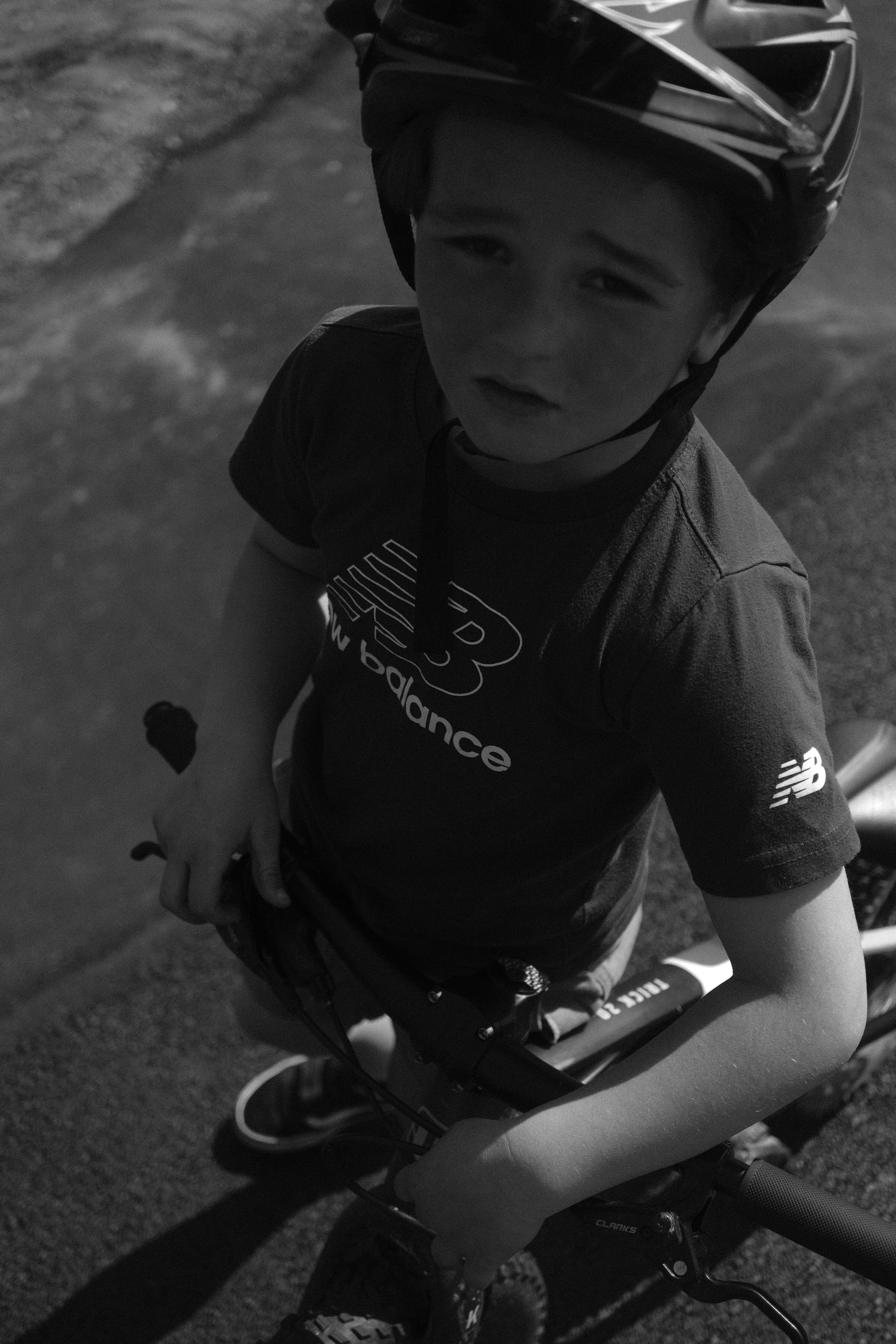 Un garçon portant un casque de vélo, debout à côté de son vélo, regardant vers le haut, en plein air.