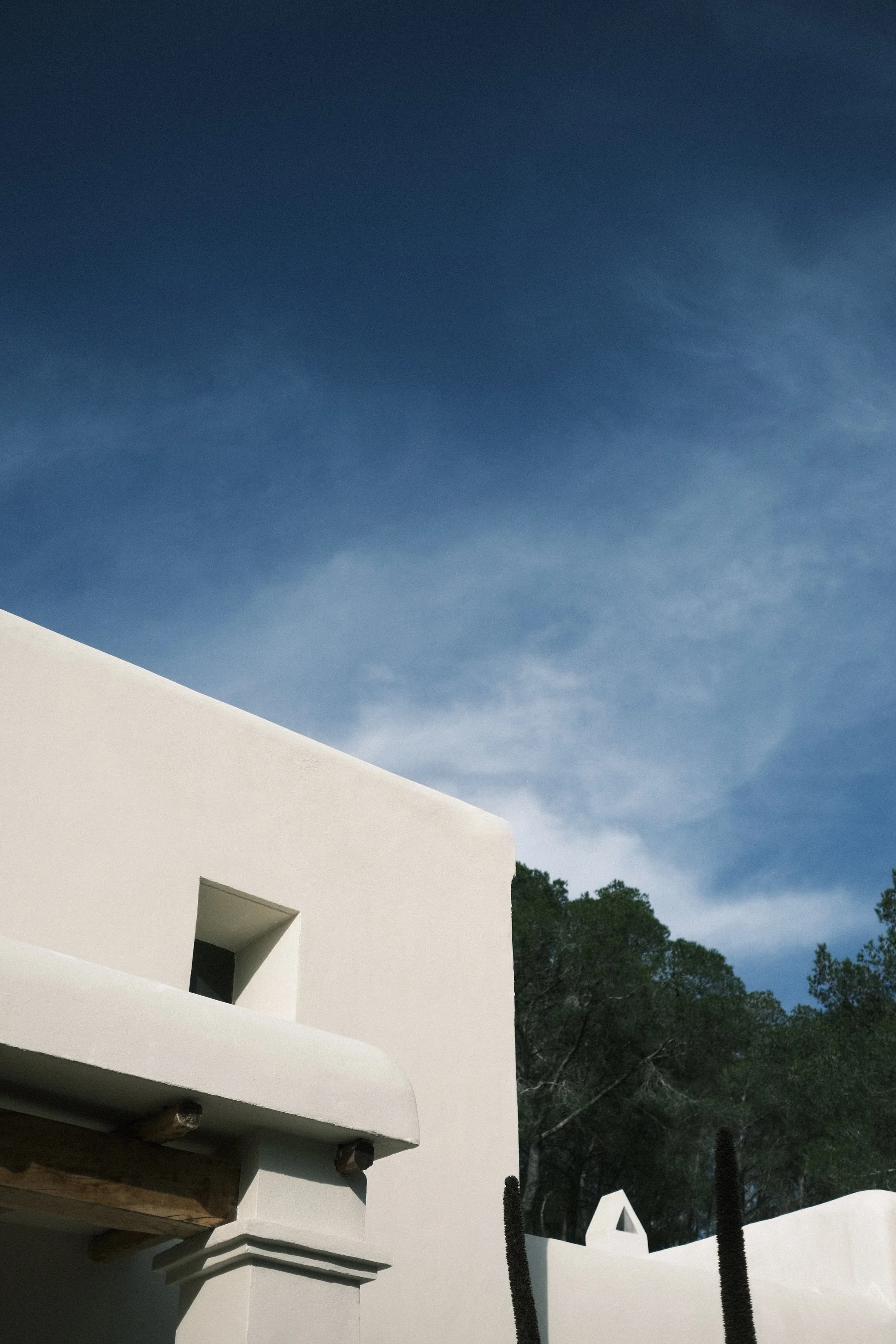 Bâtiment blanc au style moderne avec un ciel bleu et quelques arbres en arrière-plan.