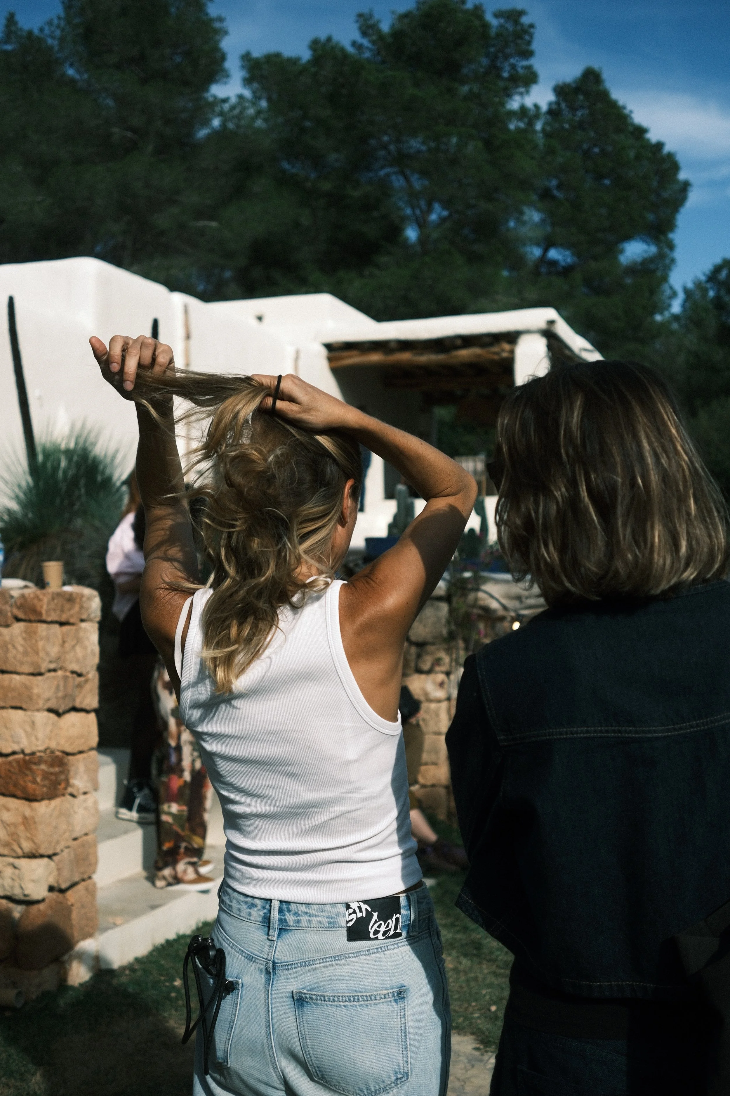 Deux femmes tournant leurs cheveux, en plein air en soirée, avec une maison blanche en arrière-plan.