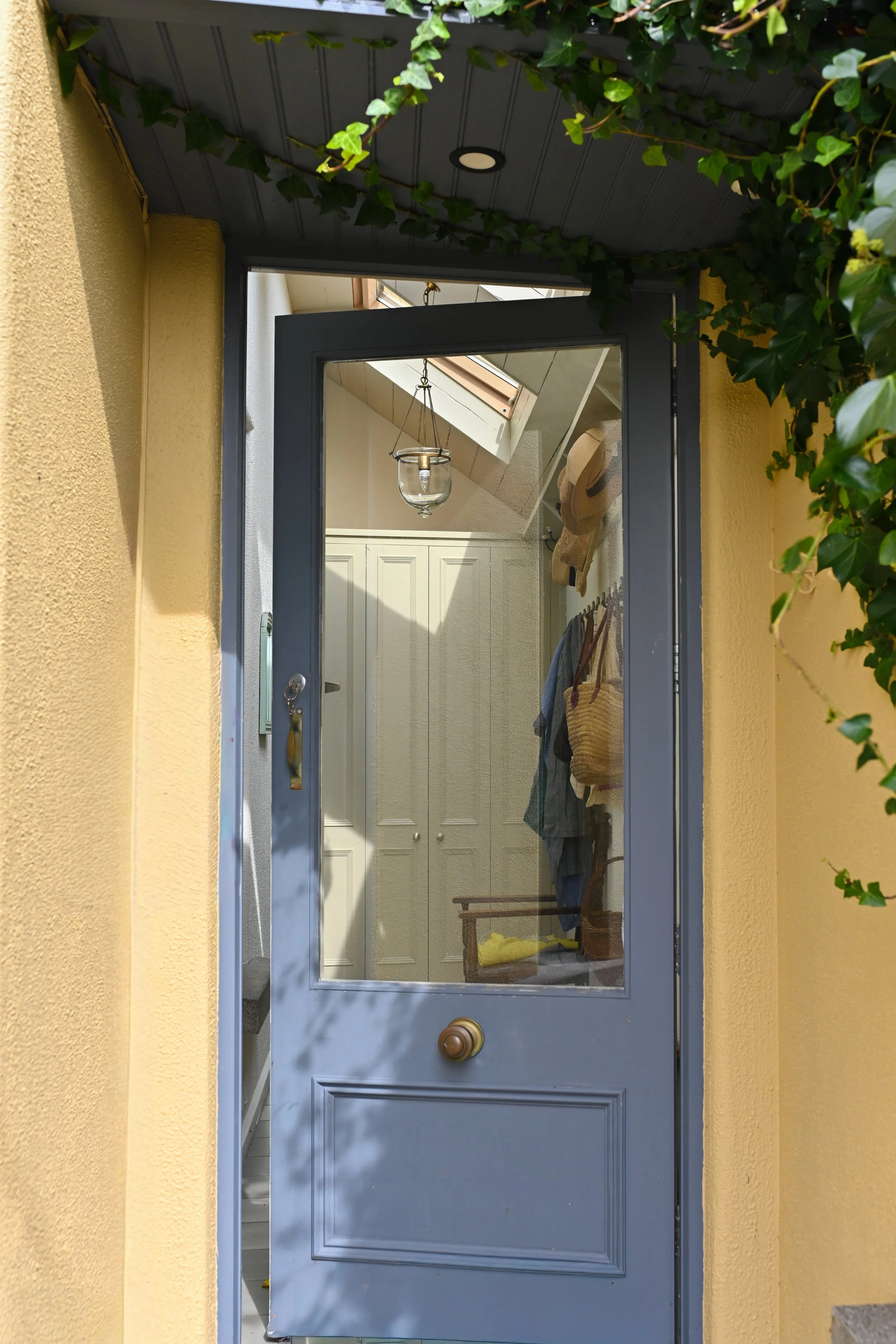 View of a blue front door with a glass window, leading into a cozy interior with a coat rack, closet, and a ceiling light fixture.