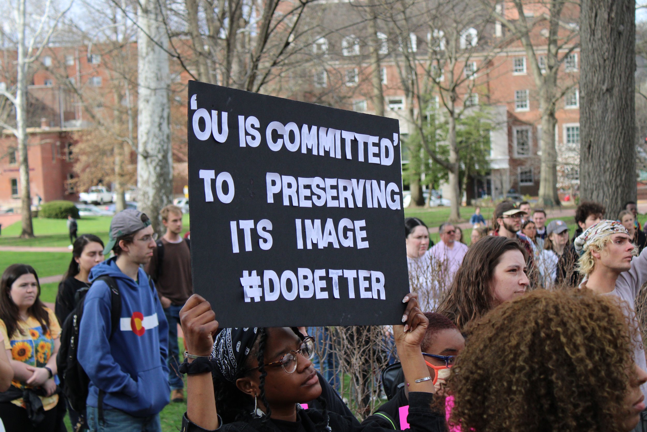  Diamond Brooks holds a sign that says “‘OU is committed’ to preserving its image #dobetter,” while listening to speakers. Photo by Izzy Keller. 