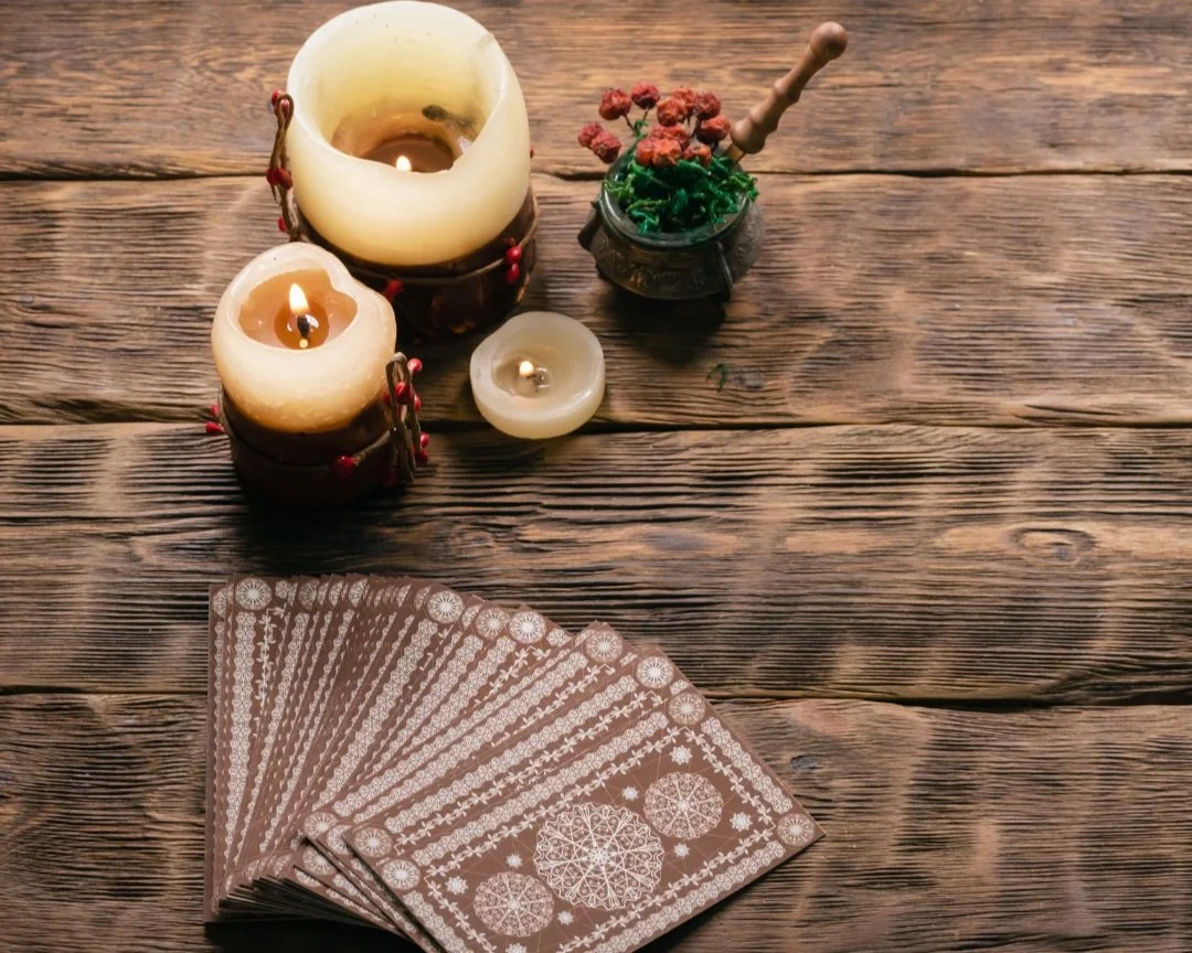 Three candles burning grouped together on a wooden table. A deck of tarot cards spread out beside it.