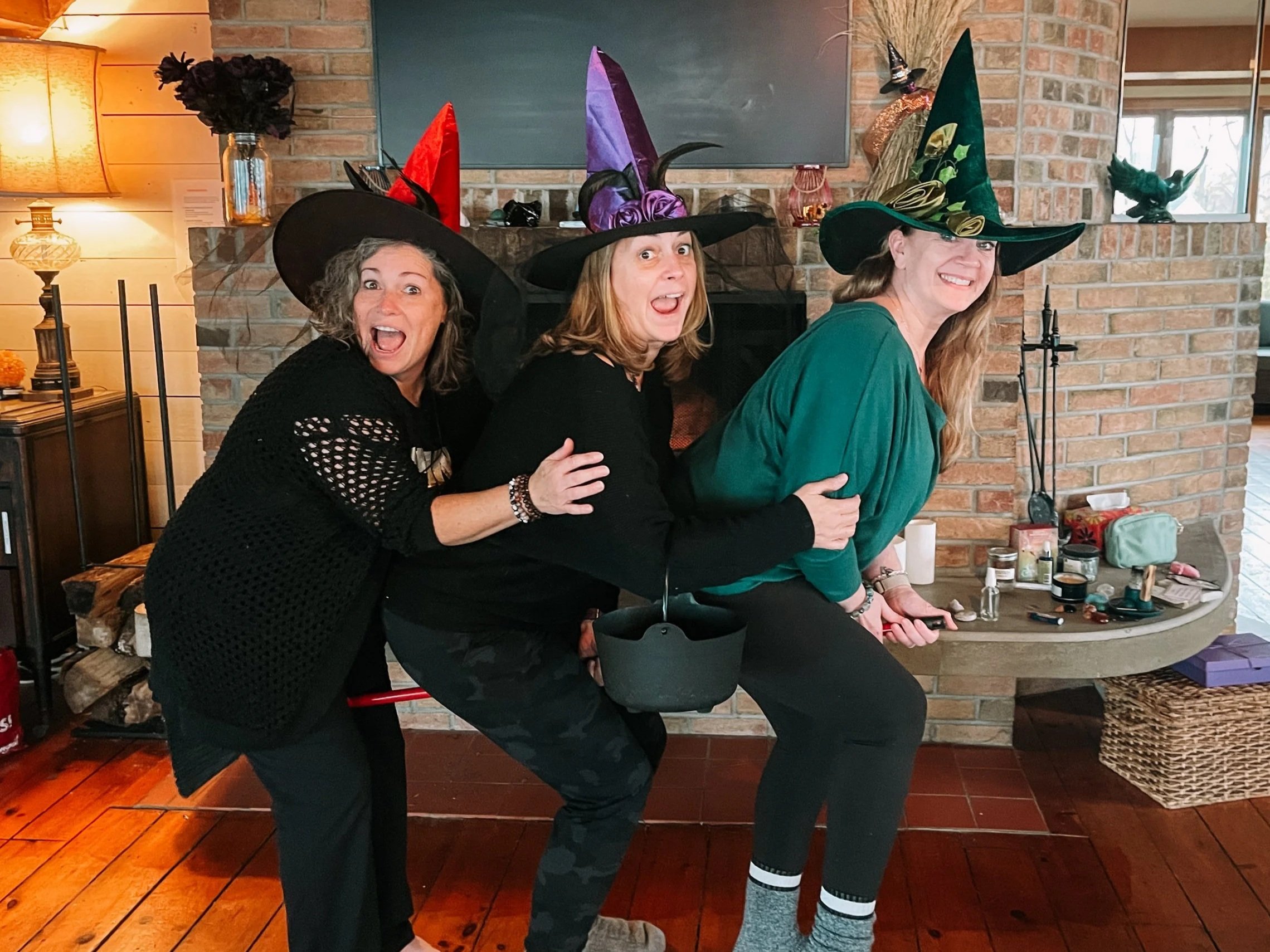 Three women wearing colourful witch hats, pretending to ride a broom.