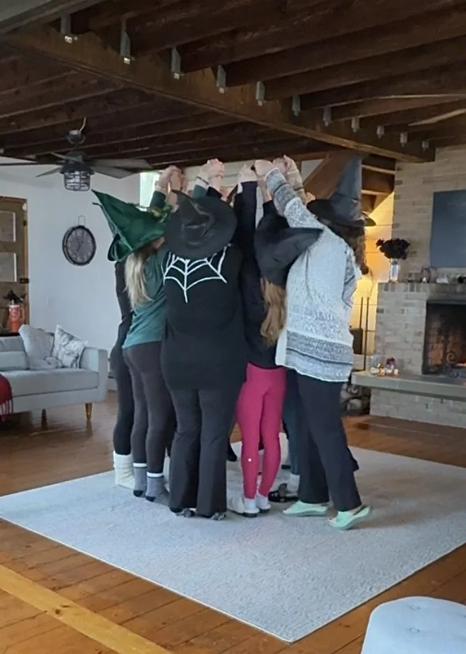 Women gather in a circle and hold their arms in the air holding hands.