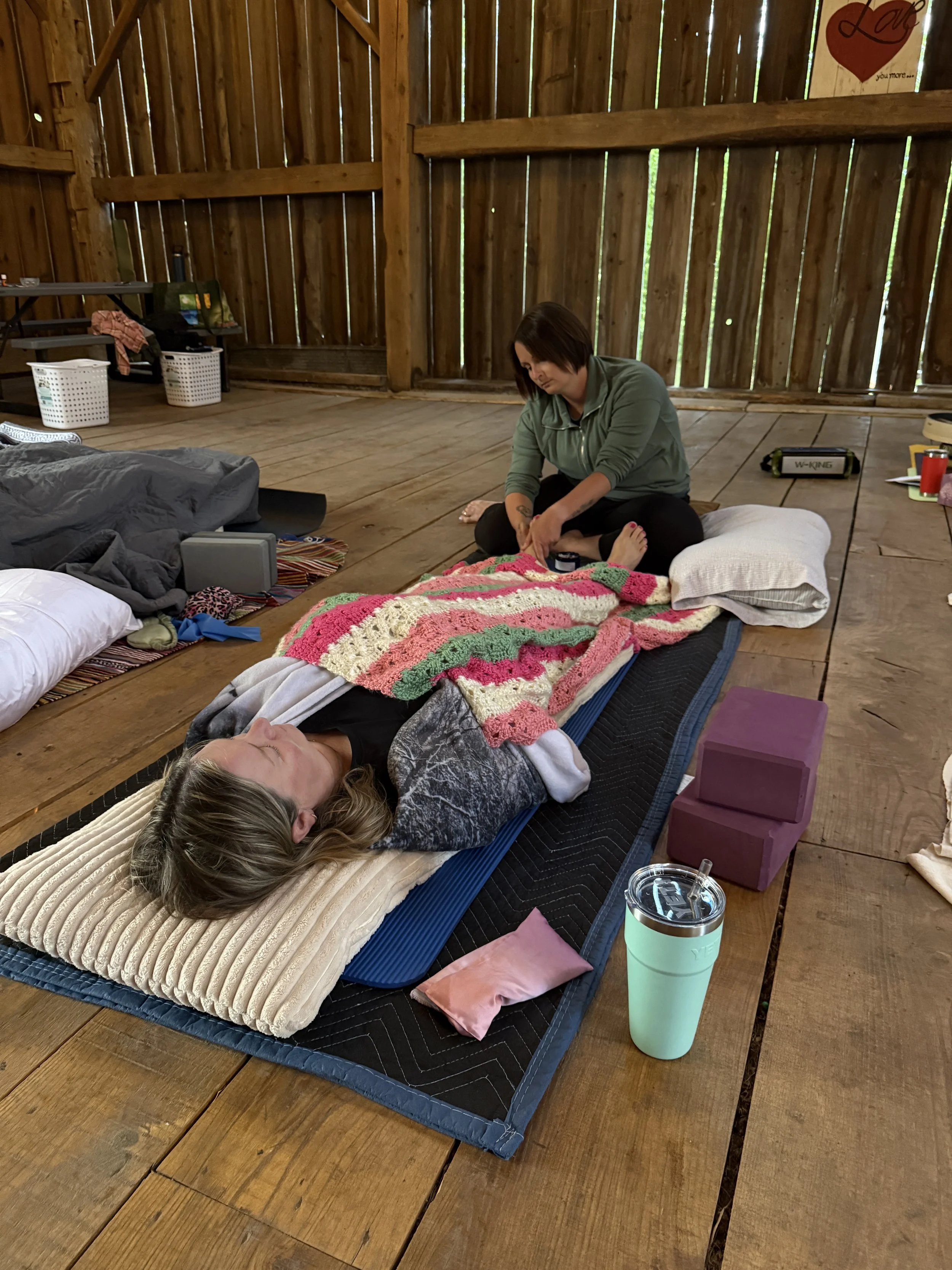 Kaylan providing a foot massage to a participant laying with blankets in a restorative position.
