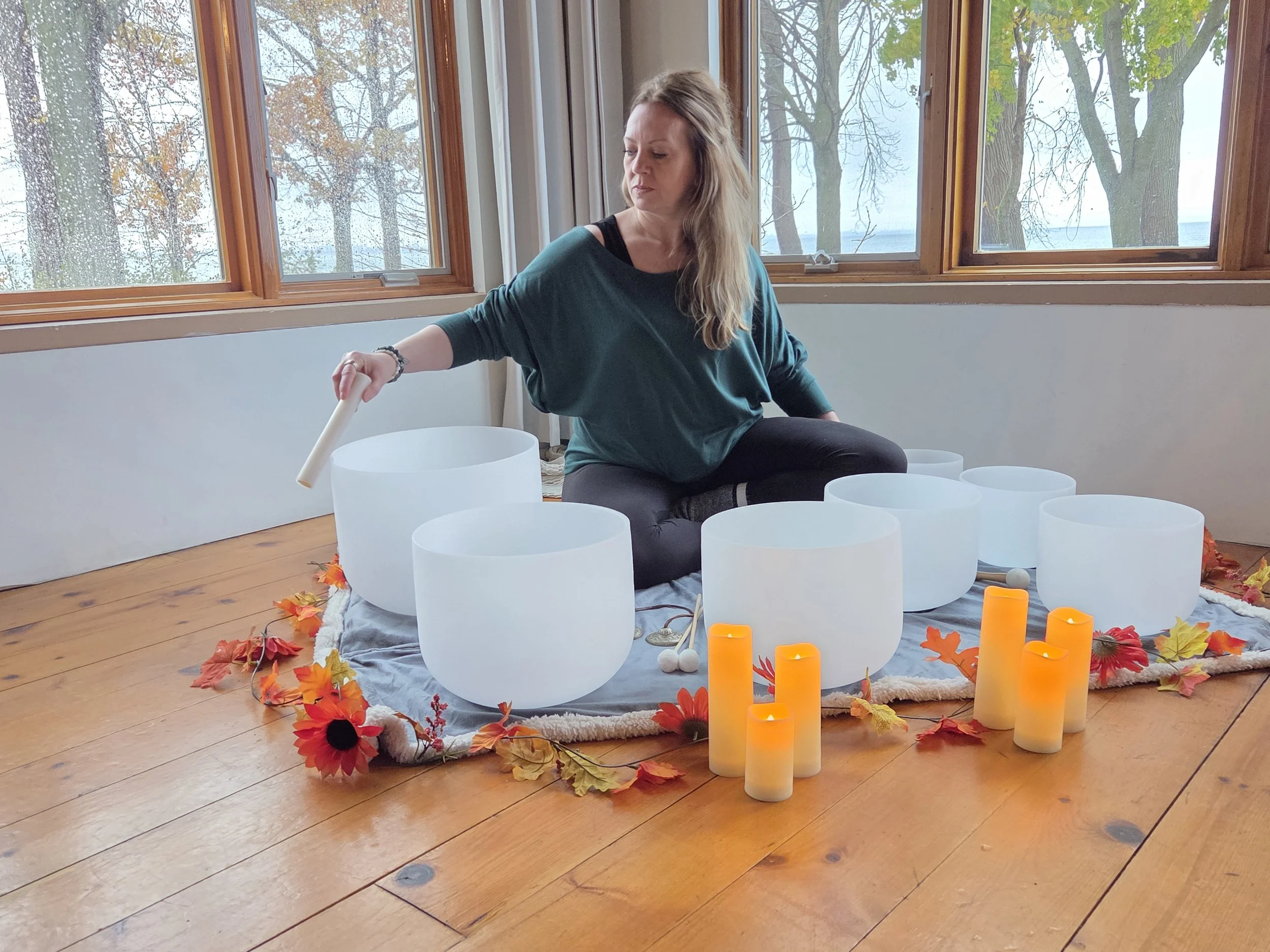 Andrea playing the sound bowl with autumn decor and candles around her.
