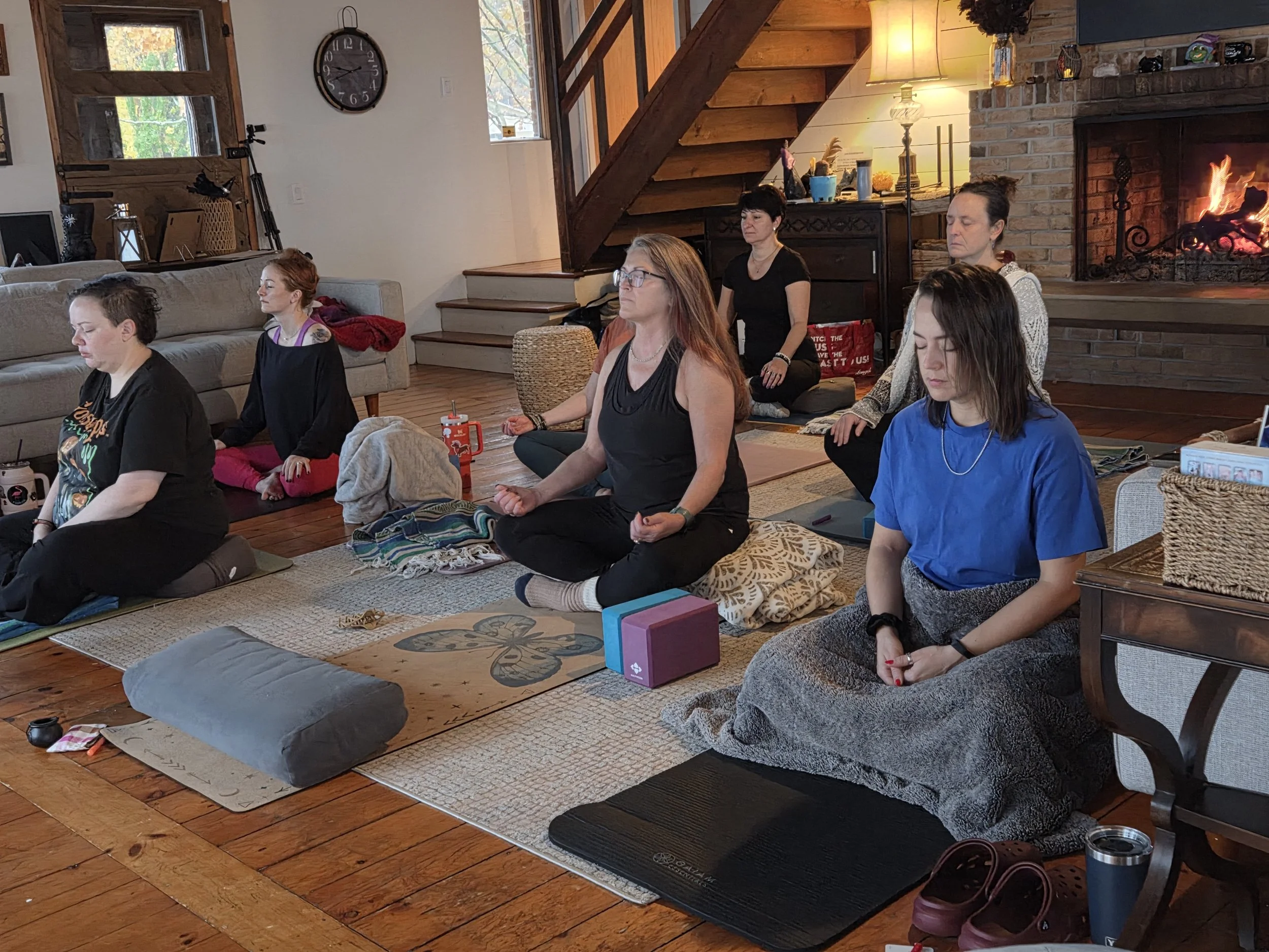 Women sitting on the yoga mats in seated meditation. A fire warm fire burns in the background.