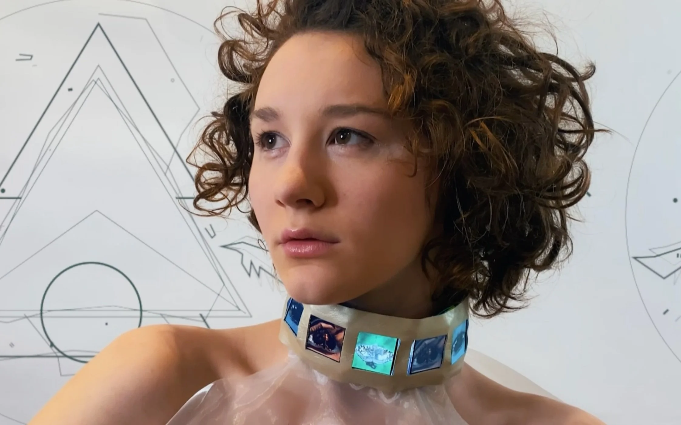 Young person with curly hair wearing a futuristic choker with digital images. Geometric designs in the background.