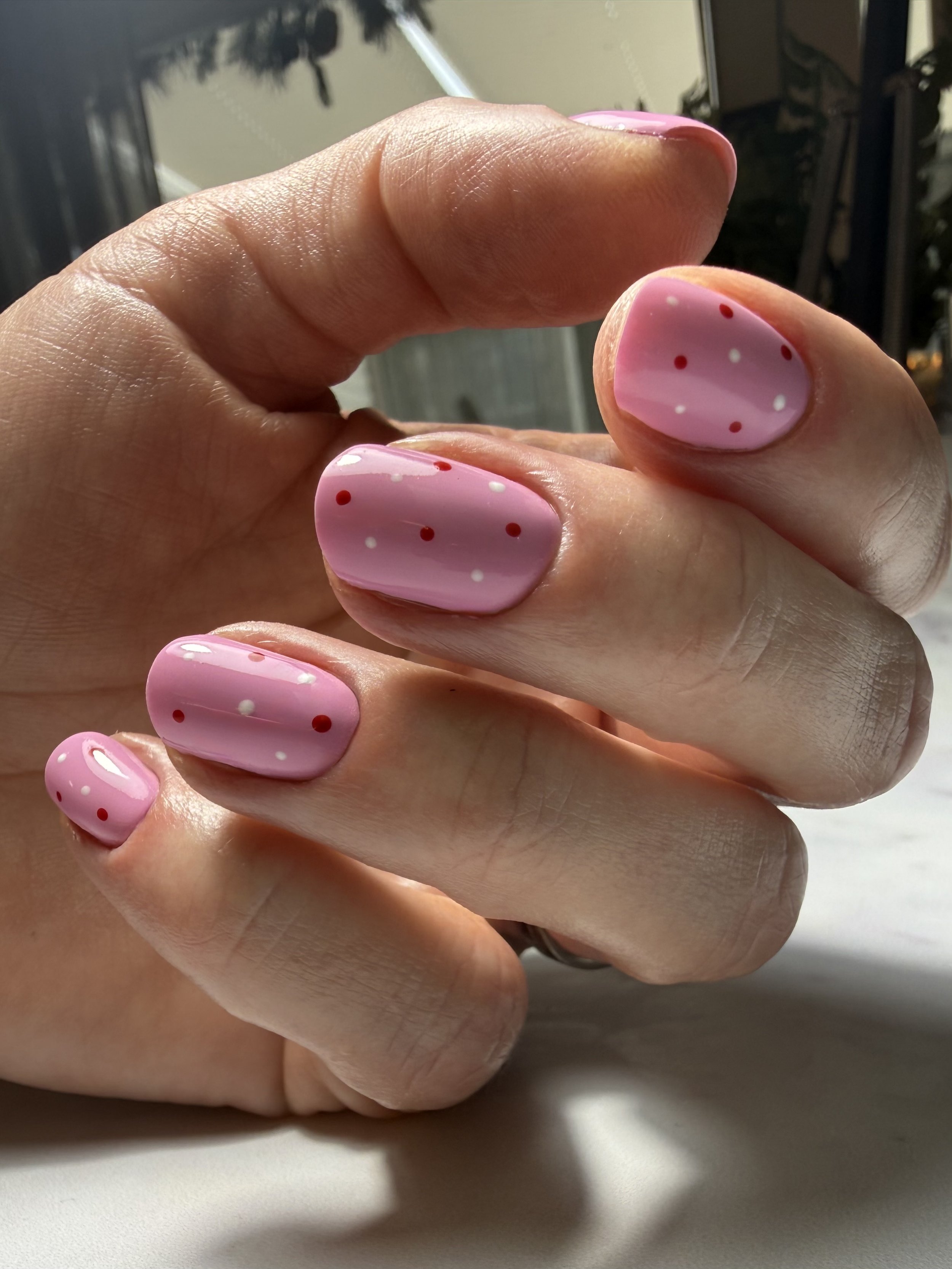 Close-up of a person's hand showcasing pink nail polish with red and white polka dots.