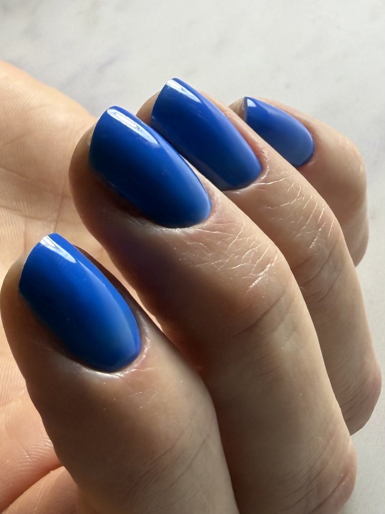 Close-up of a hand with nails painted in bright blue, shown in a slightly curled position.