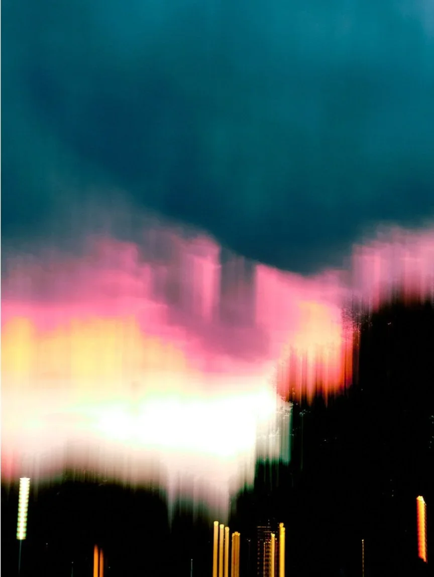 abstract neon blue, pink and yellow over a large black shadow. a blurry city scape.