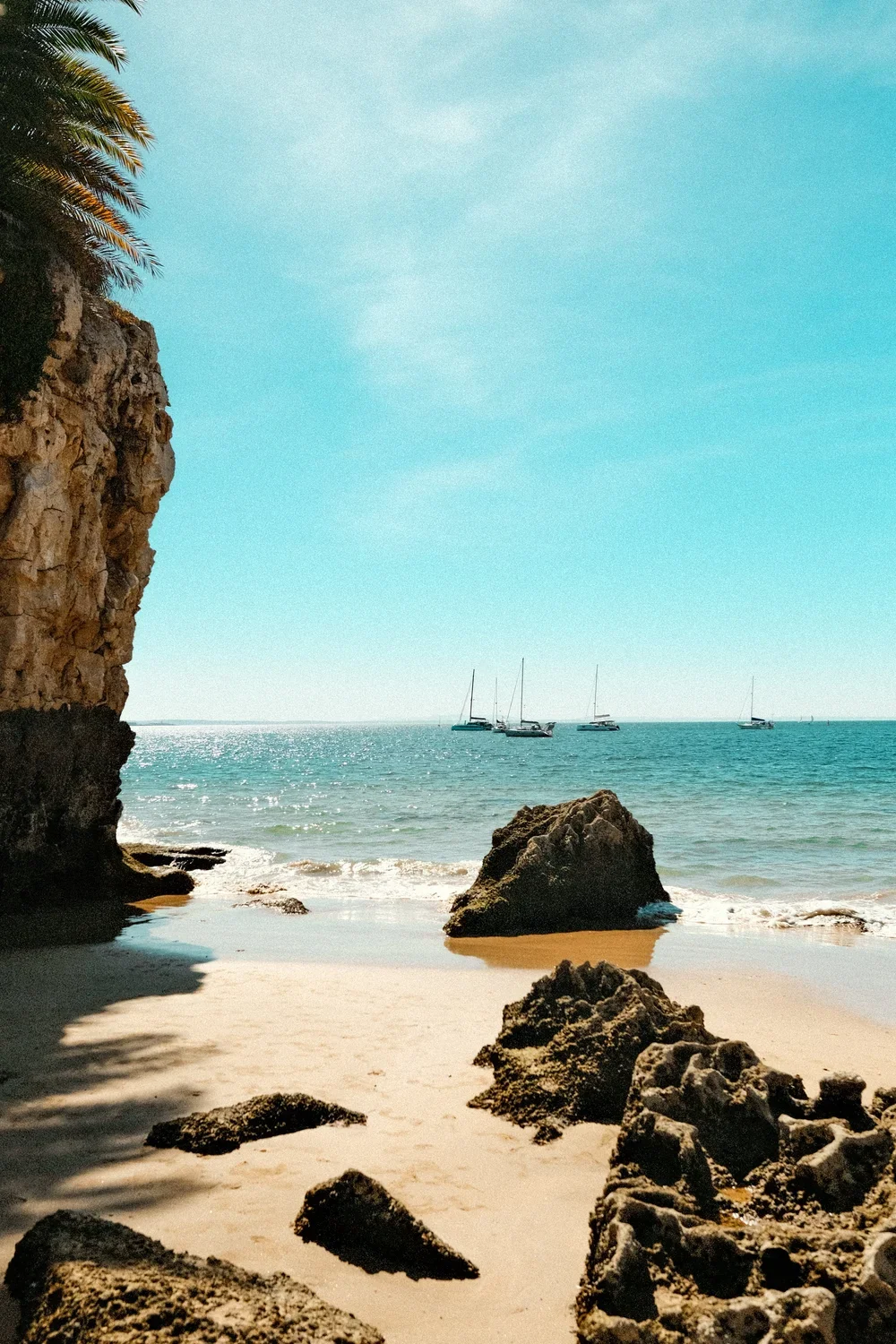 four boats on the seaside photographed from the beach with rocks in the foreground.