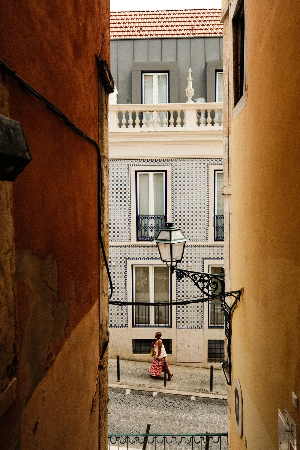 photograph of a woman walking visible through the alleyway of a street in Lisbon portugal
