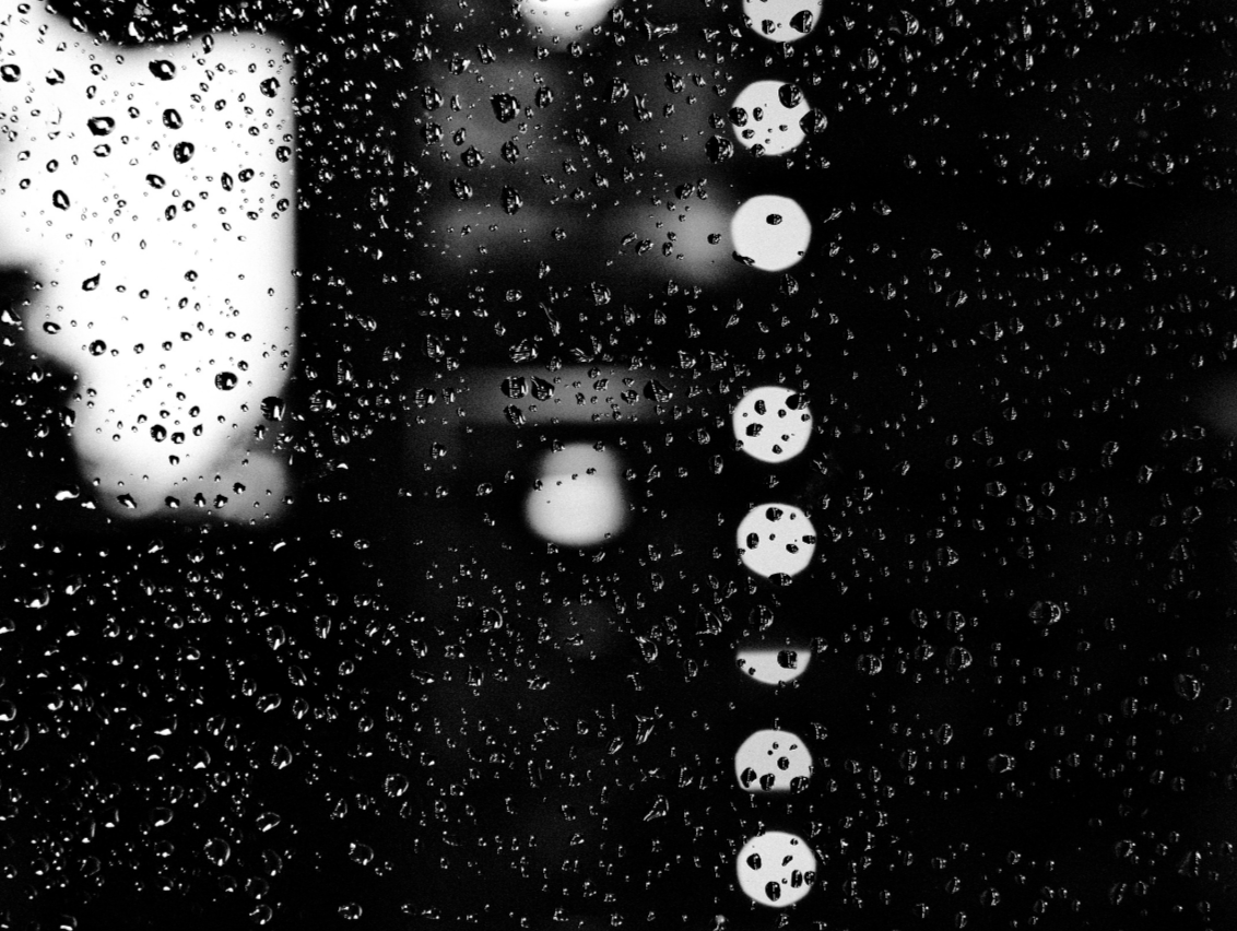 Close-up of raindrops on a glass window with blurred city lights in the background.