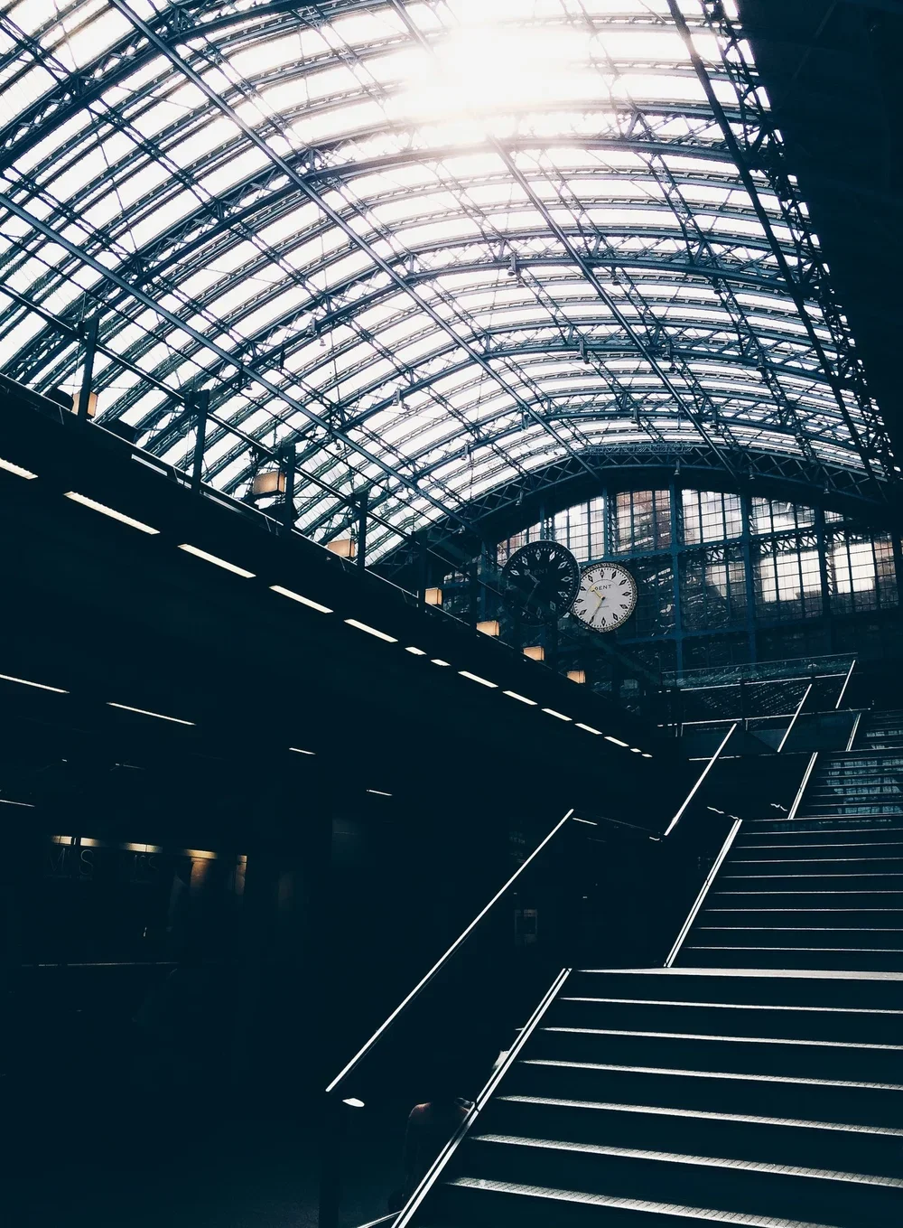 photography of a staircase up towards a glass ceiling with a large clock