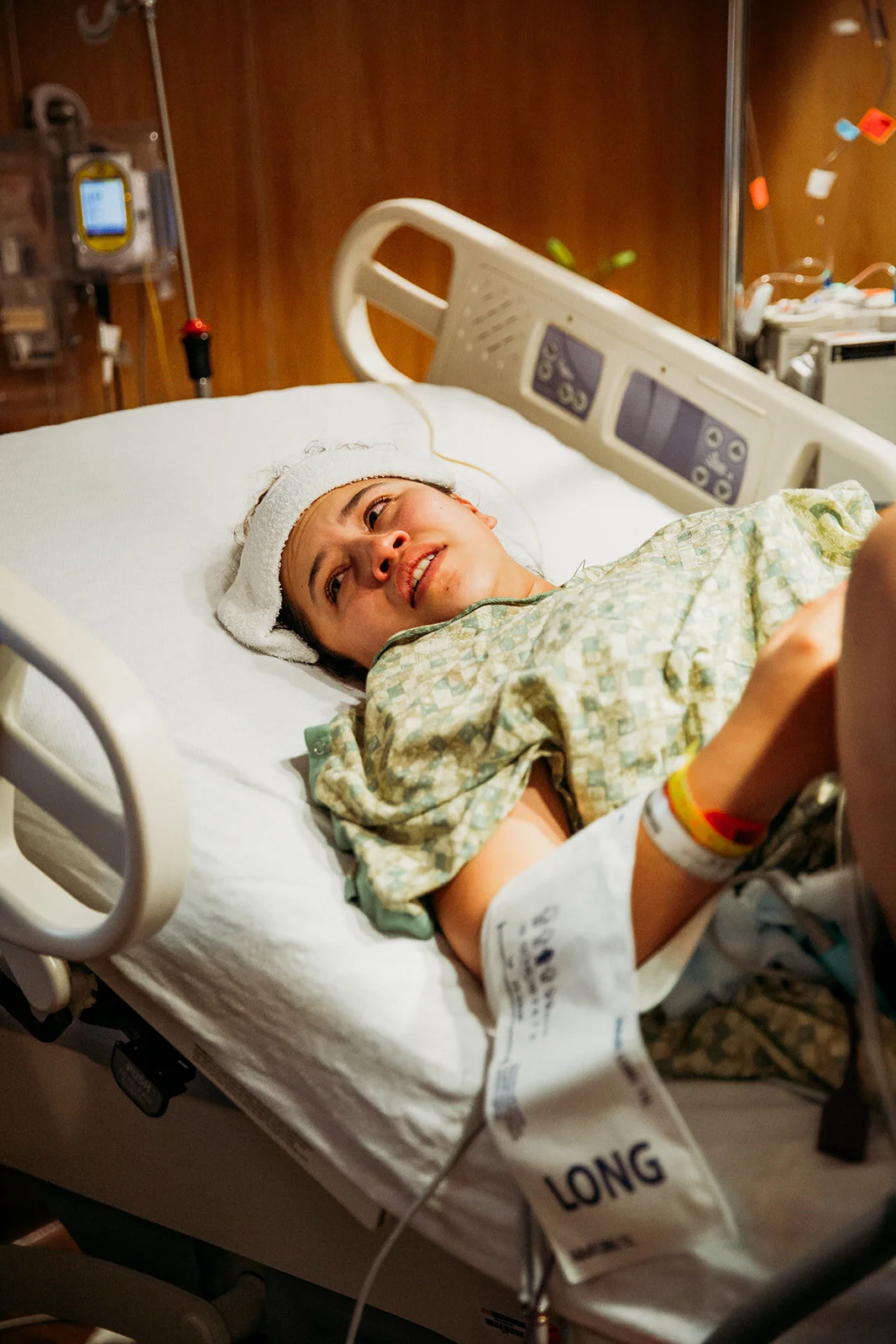a mother with tears in her eyes looks left out of frame where her newborn is being examined following birth | Odessa regional medical center birth photography
