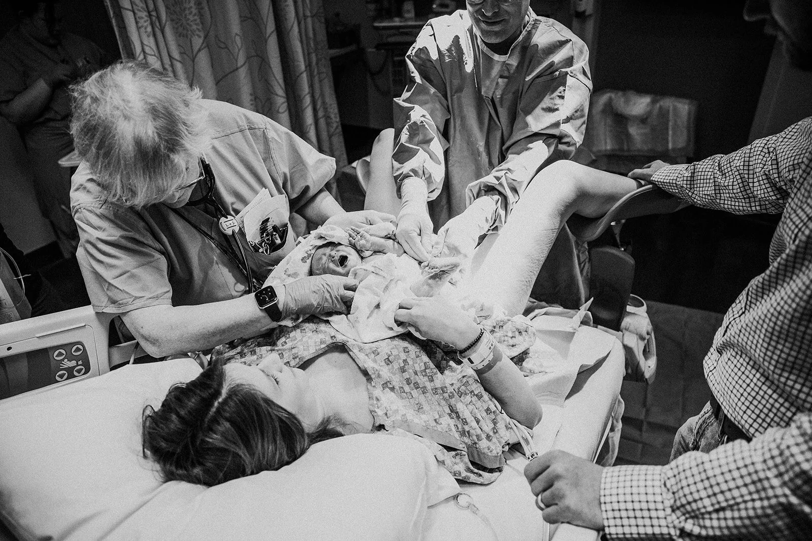 Black and white image of a newborn being laid on his mother's chest in a hospital bed immediately following birth | birth photography in the hospital