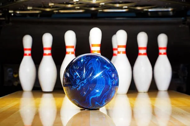 Image description: blue bowling ball in front of bowling pins on a bowling lane.