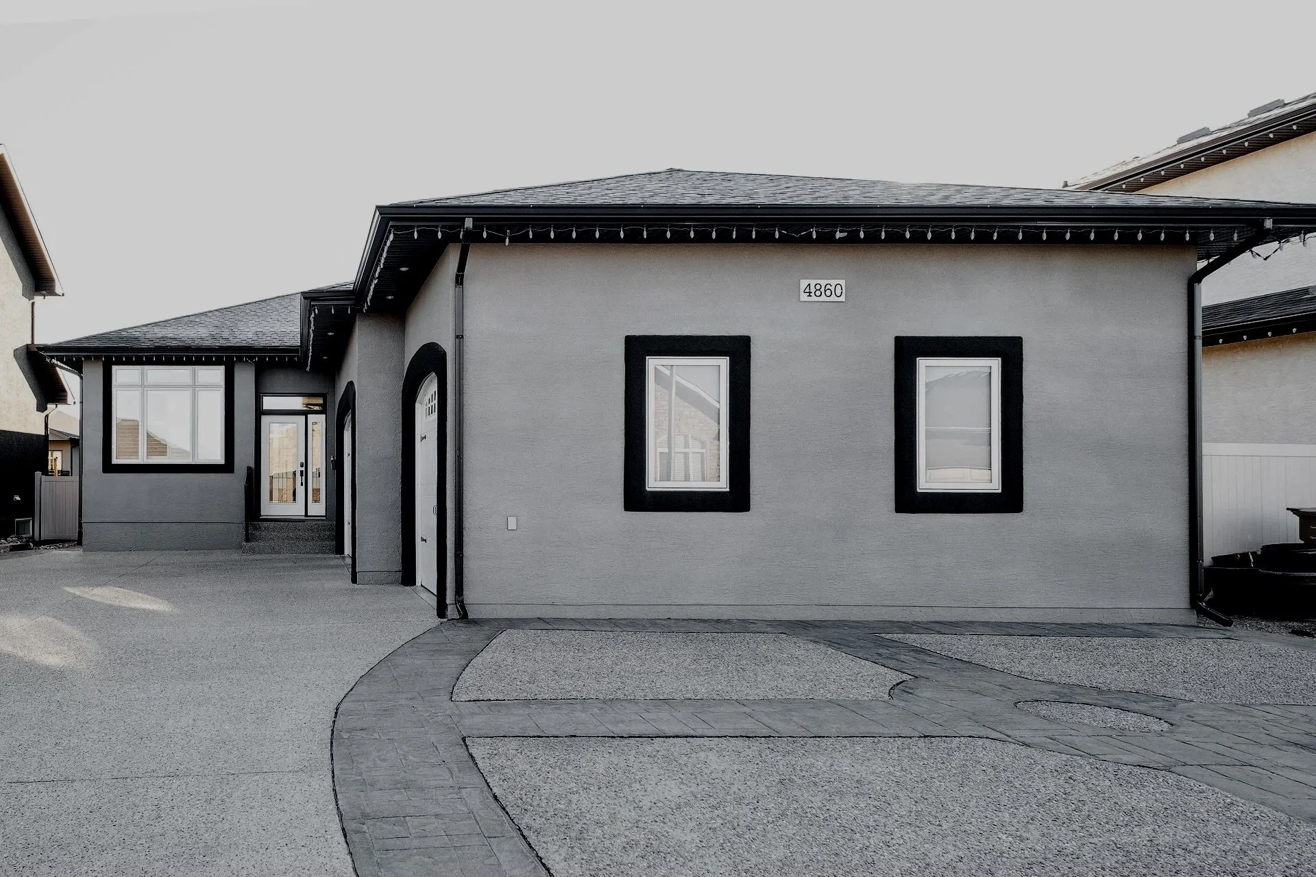 Modern gray corked house with dark trim, two rectangular windows, a garage door, and a pathway leading to the entrance.