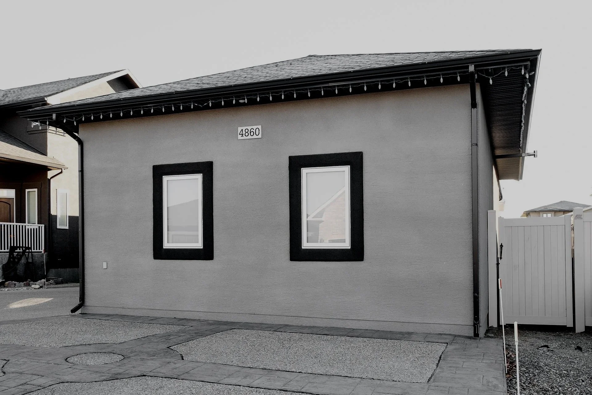 Rear view of a modern house with two windows, a house number plate, and a white fence gate on the right side.