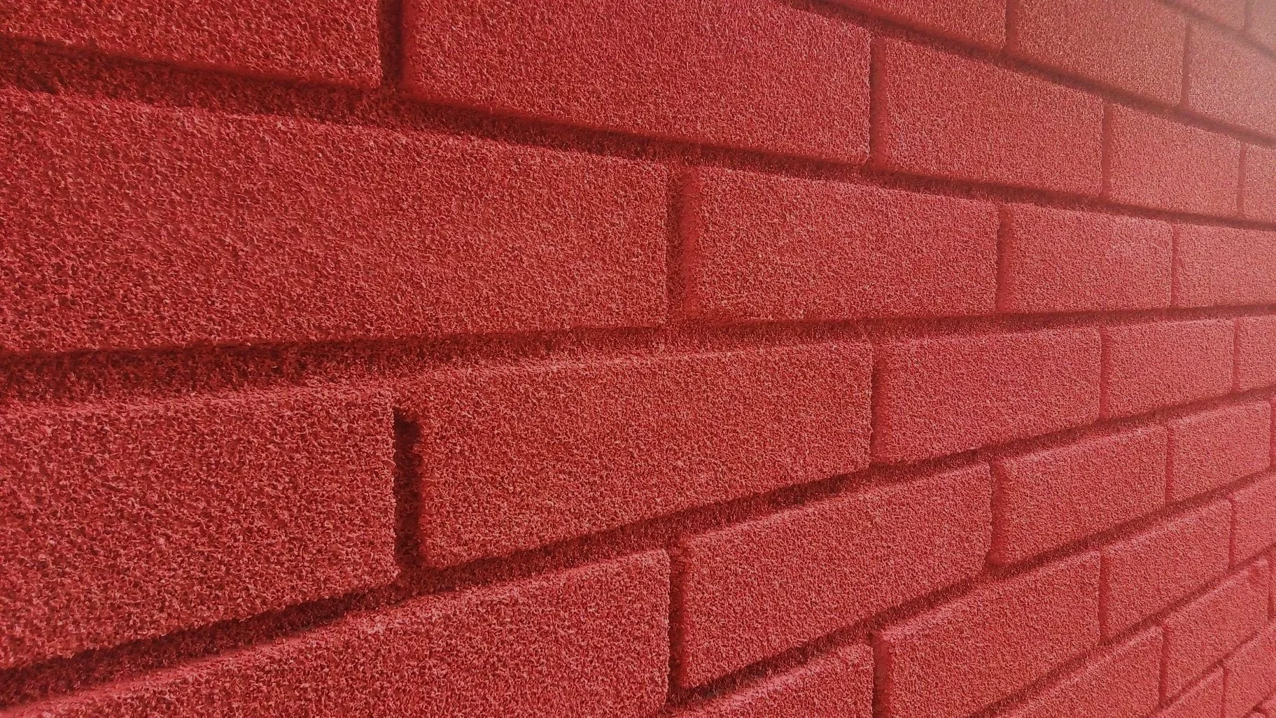 Red brick wall with textured and breathable VIPEQ cork coating surface and visible mortar lines.