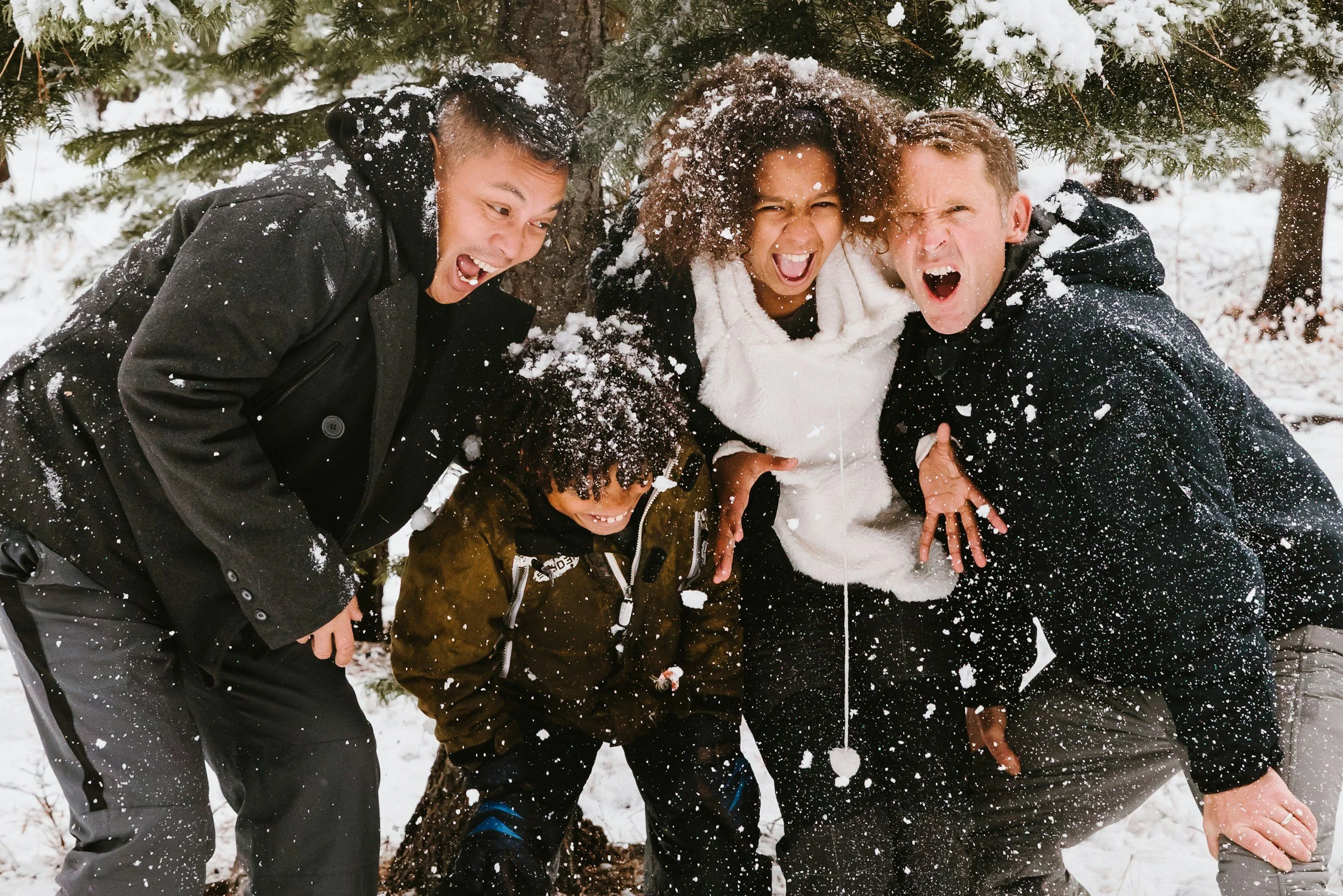 family of 4 leans in close while laughing and having fun in the snow