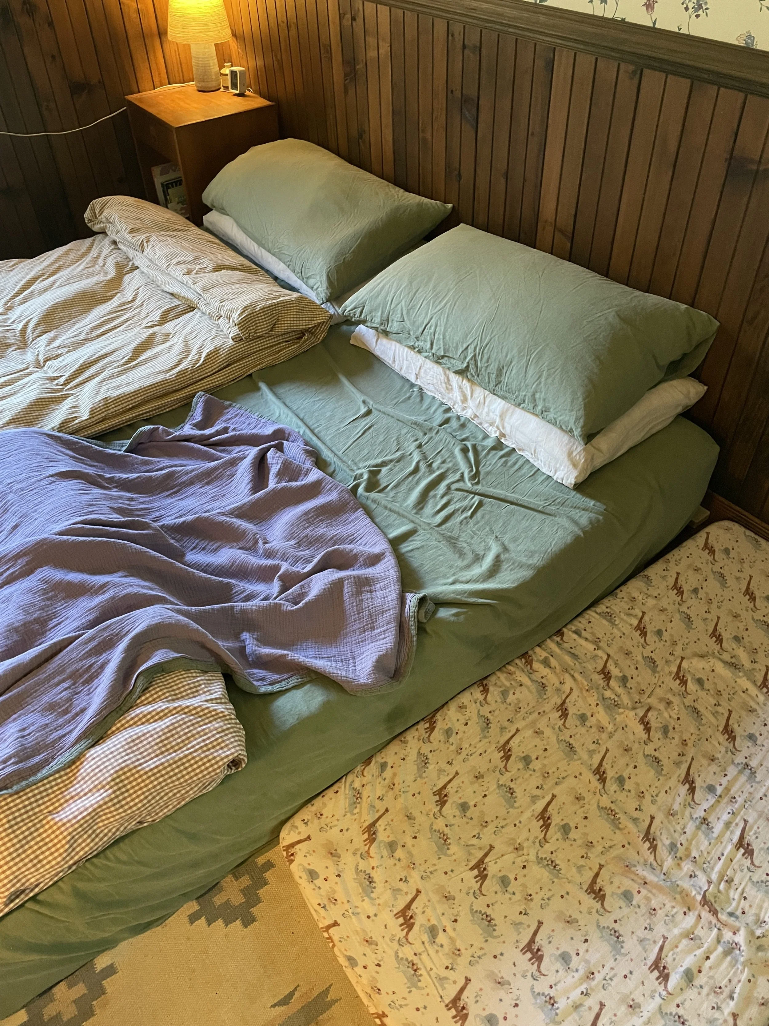 a photo of a bed set up for safe bedsharing. the mattress is on the ground with a crib mattress beside it. there are separate beddings both both adults and the sleep surface for baby is clear.