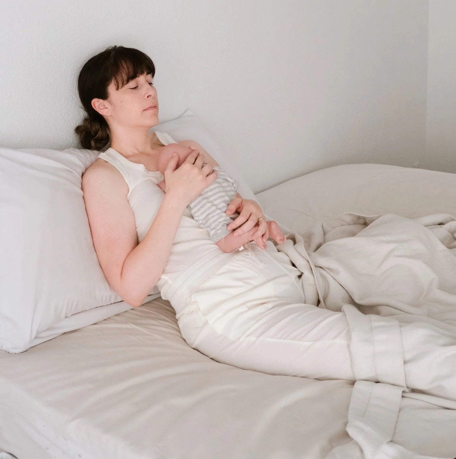 a white person sleeps in a reclined position with a baby on their chest
