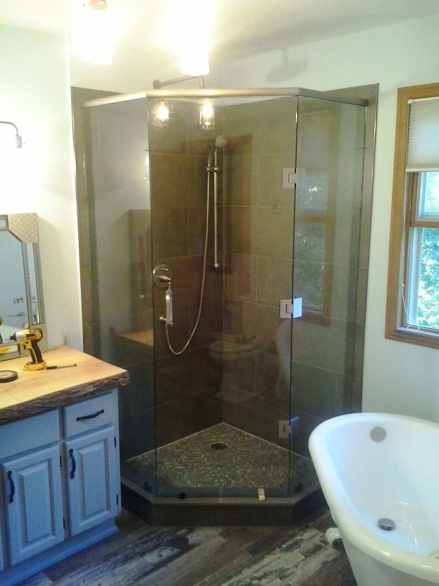 Bathroom with a glass shower enclosure, a wooden vanity with a drill on the countertop, a window with blinds, and a bathtub.