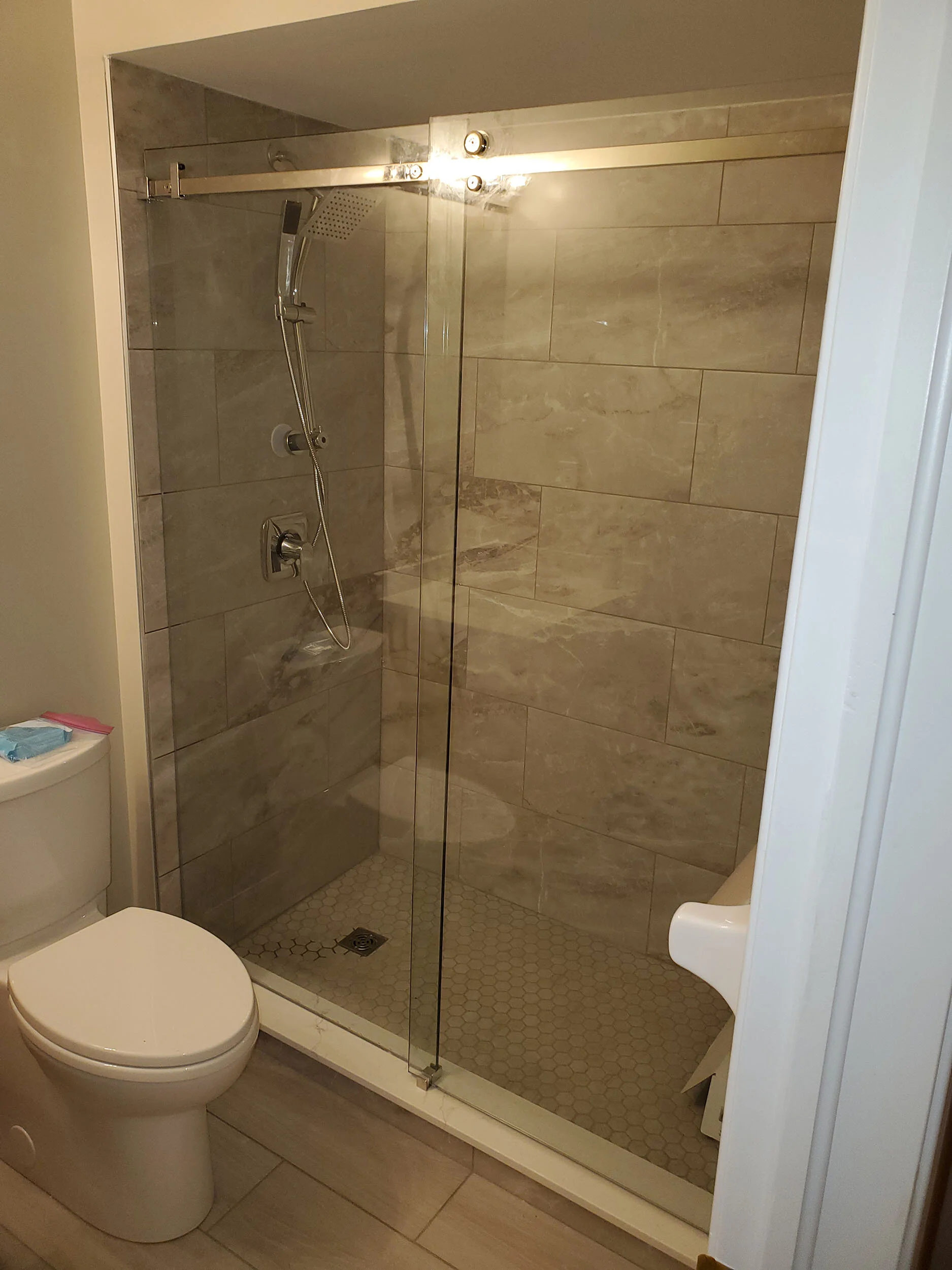 A bathroom with a glass-enclosed shower, toilet, and a small stool or chair.