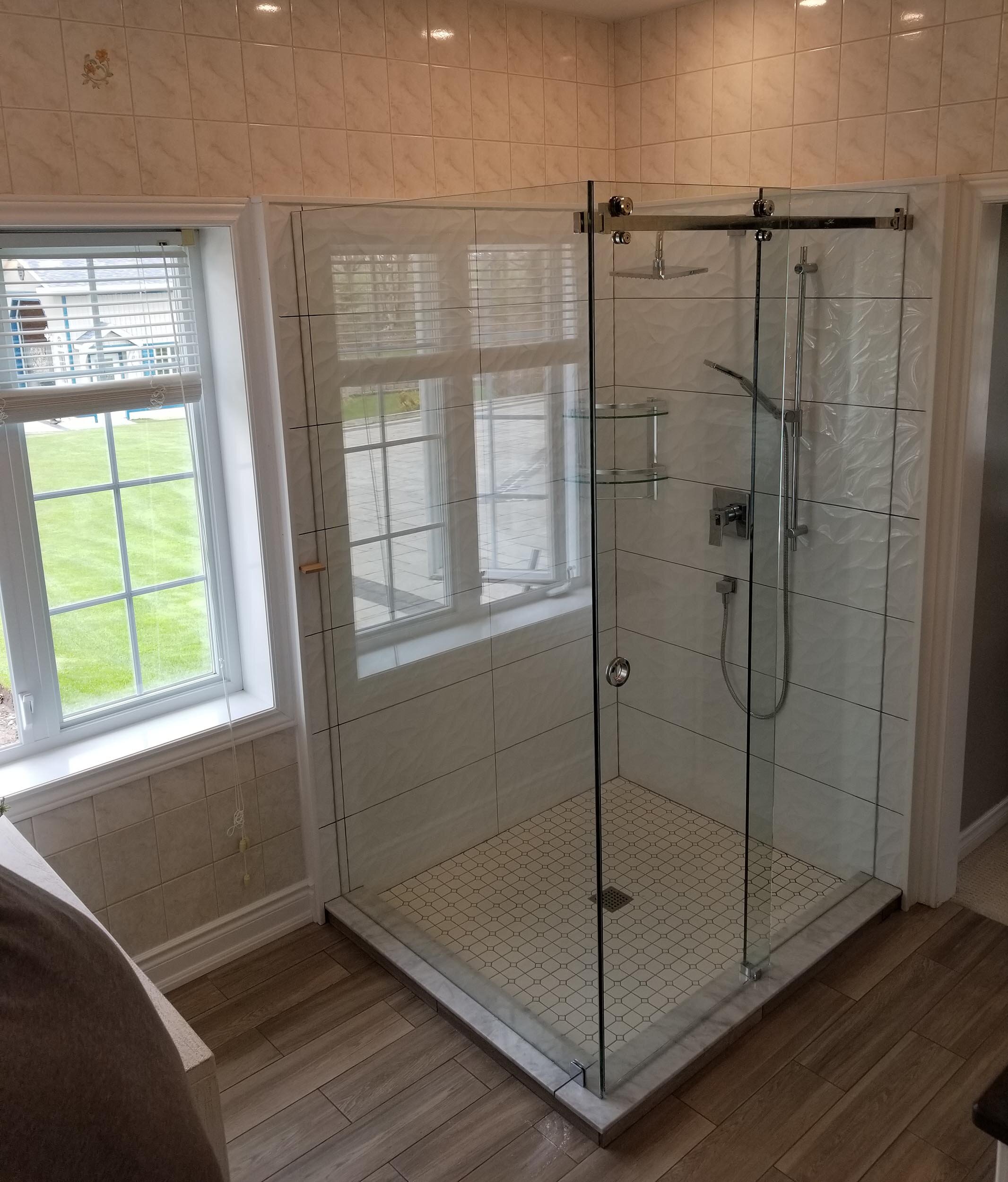 A glass shower enclosure with a tiled floor in a bathroom next to a window.