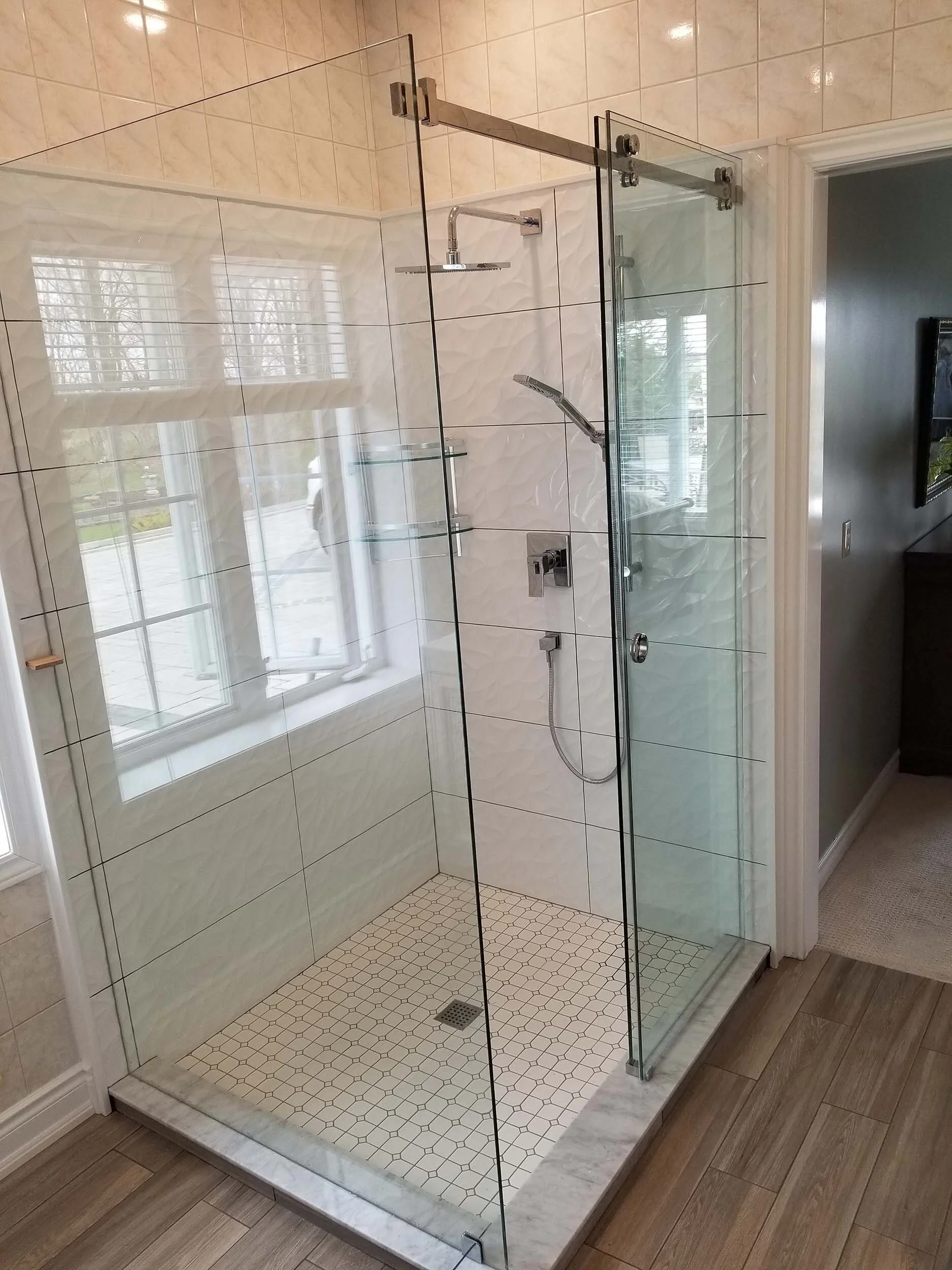 Glass-enclosed shower with white textured tiles, a window, and bathroom fixtures inside.