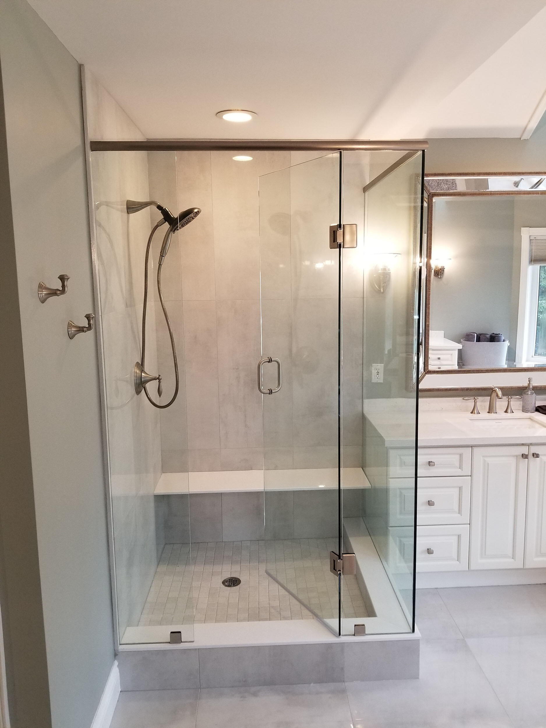 A modern bathroom with a glass-enclosed shower, white vanity with a mirror, and a window.