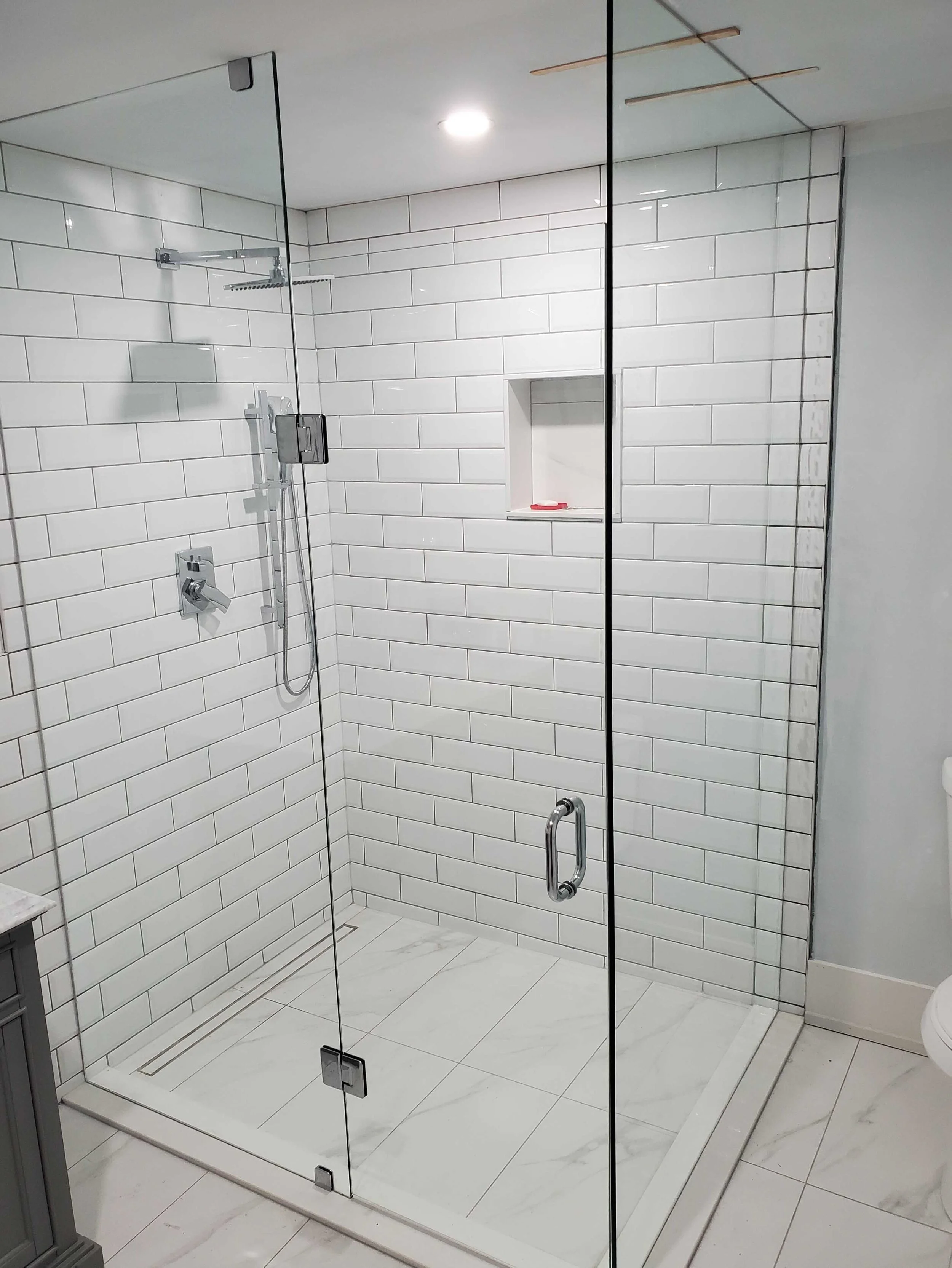 Clean glass shower enclosure with white subway tiles and a built-in niche for toiletries, with a marble tiled floor and a built-in shower head.