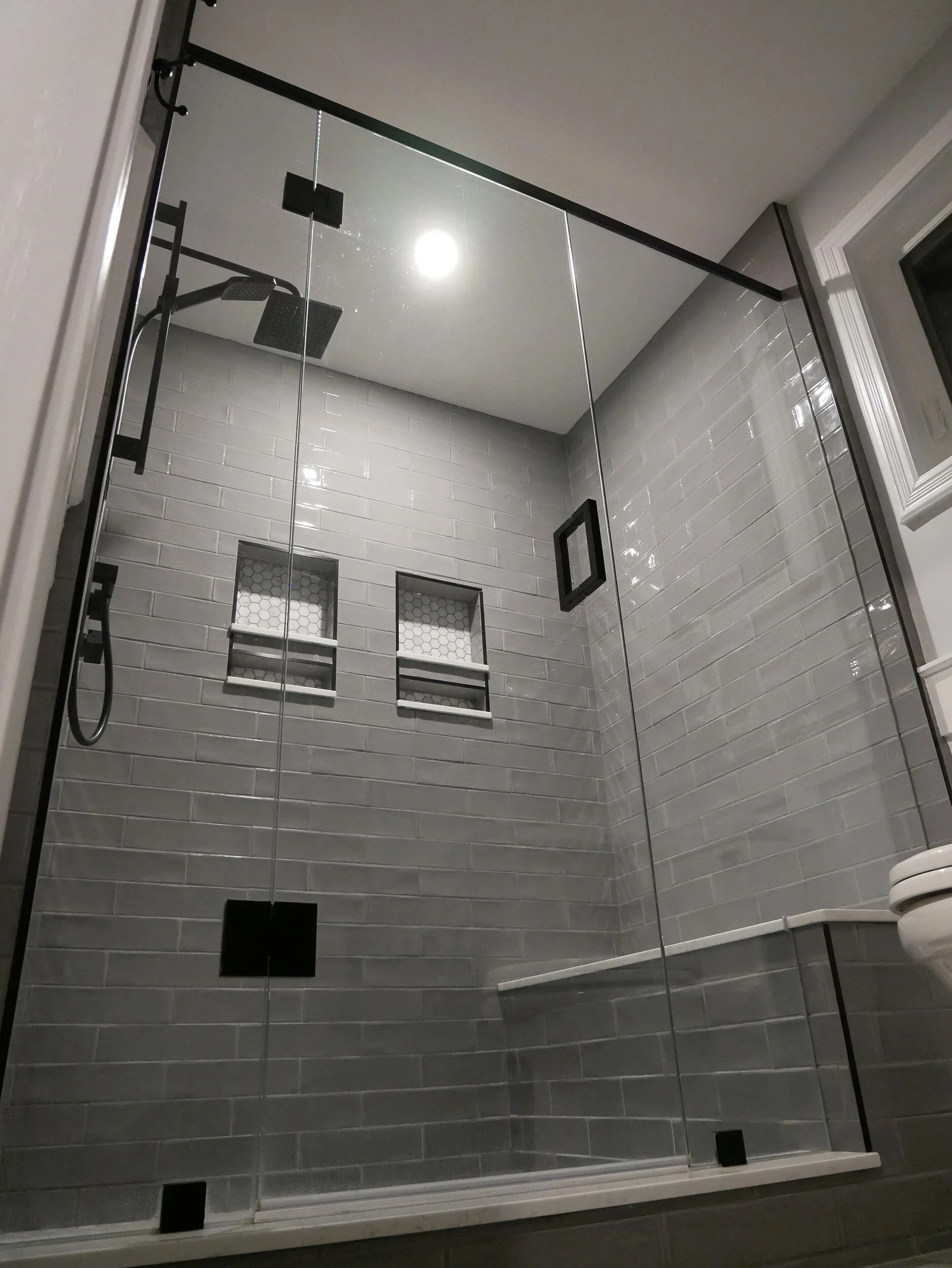 Modern glass-enclosed shower with gray tiled walls, built-in niche shelves, a rainfall showerhead, and a hand-held shower.