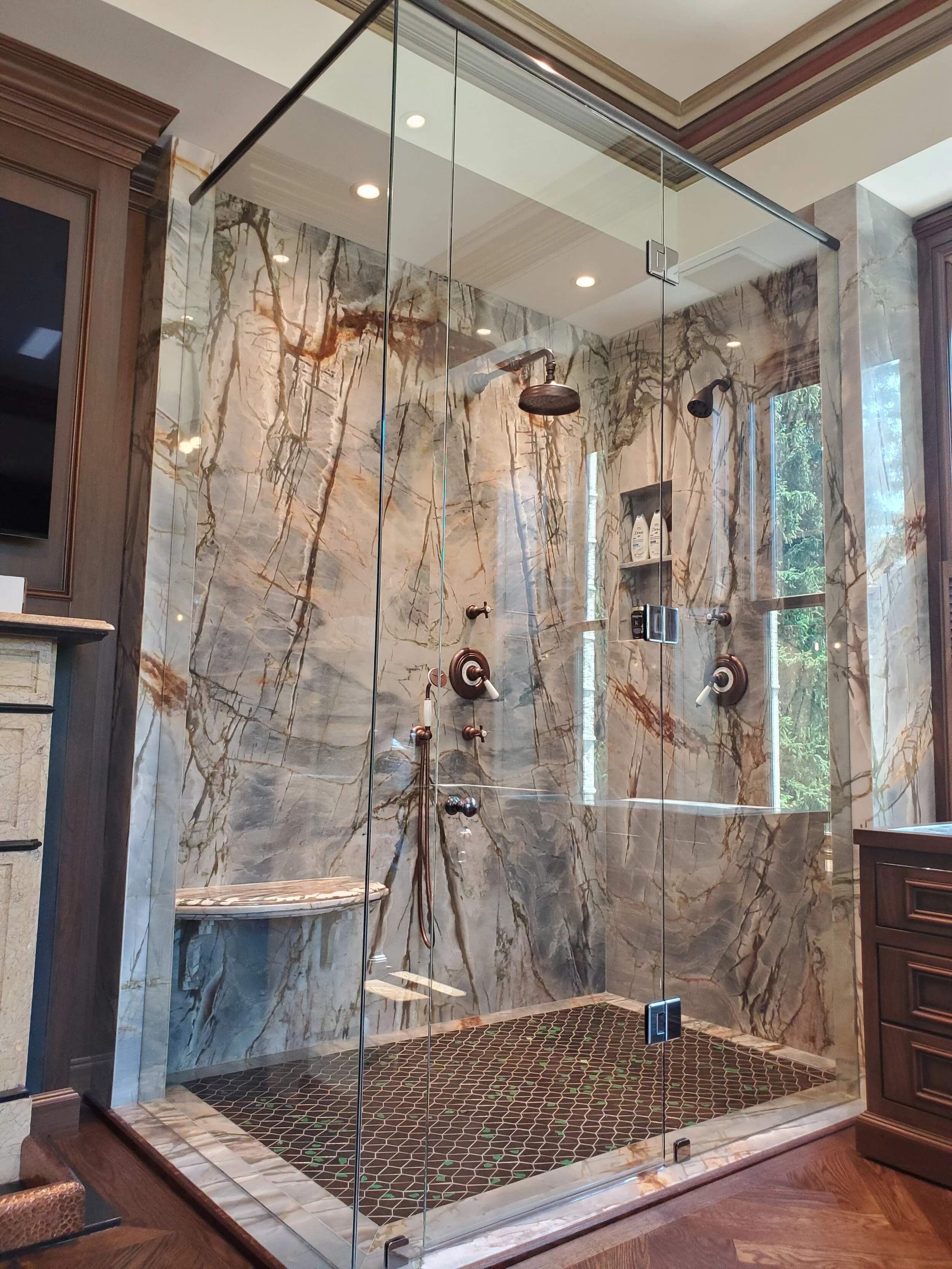 A luxurious walk-in shower with large marble walls, two showerheads, a handheld shower, and a built-in bench, enclosed with glass panels.
