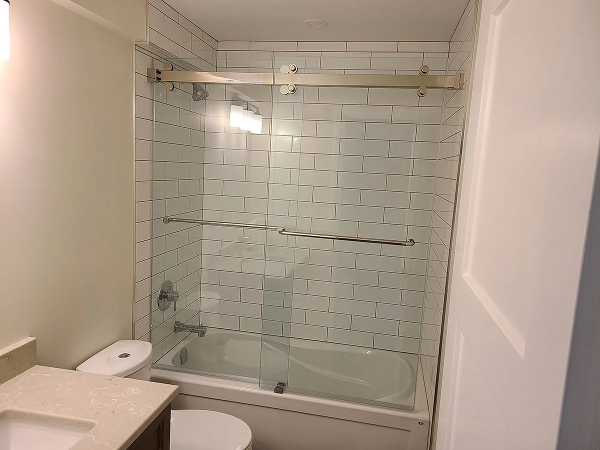 Bathroom with bathtub, glass sliding door, white subway tile wall, and toilet.