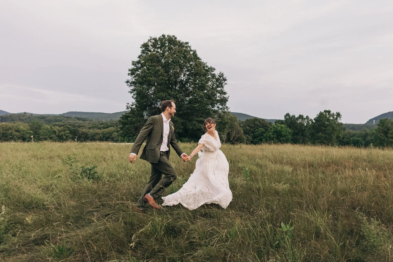 A bride and groom run through a meadow after their wedding at the Red Barn at Hampshire College in Amherst, Massachusetts.