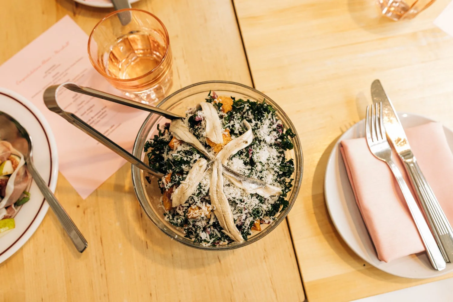 A caeser salad with anchovies is set down on a tablescape during a small wedding at Juliet in Somerville, Massachusetts.