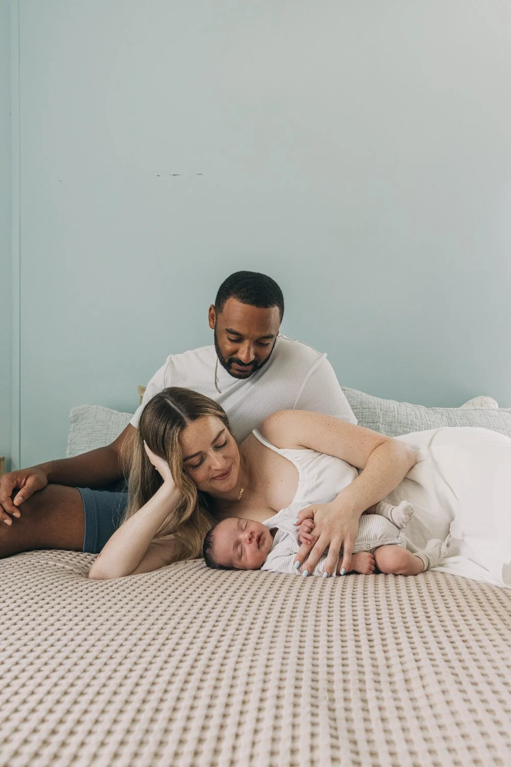 A couple lays with their newborn baby on their bed during a newborn phtoography session in western massachusetts.