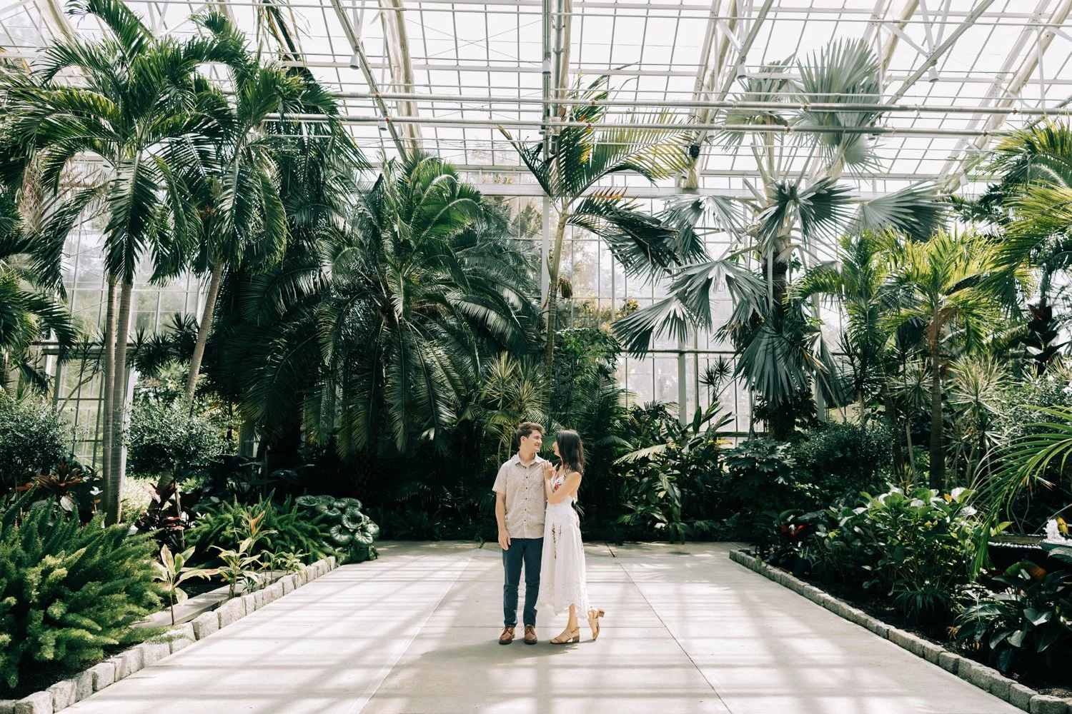 A couple stands in the greenhouse at roger williams park in rhode island for their rhode island engagement photos.